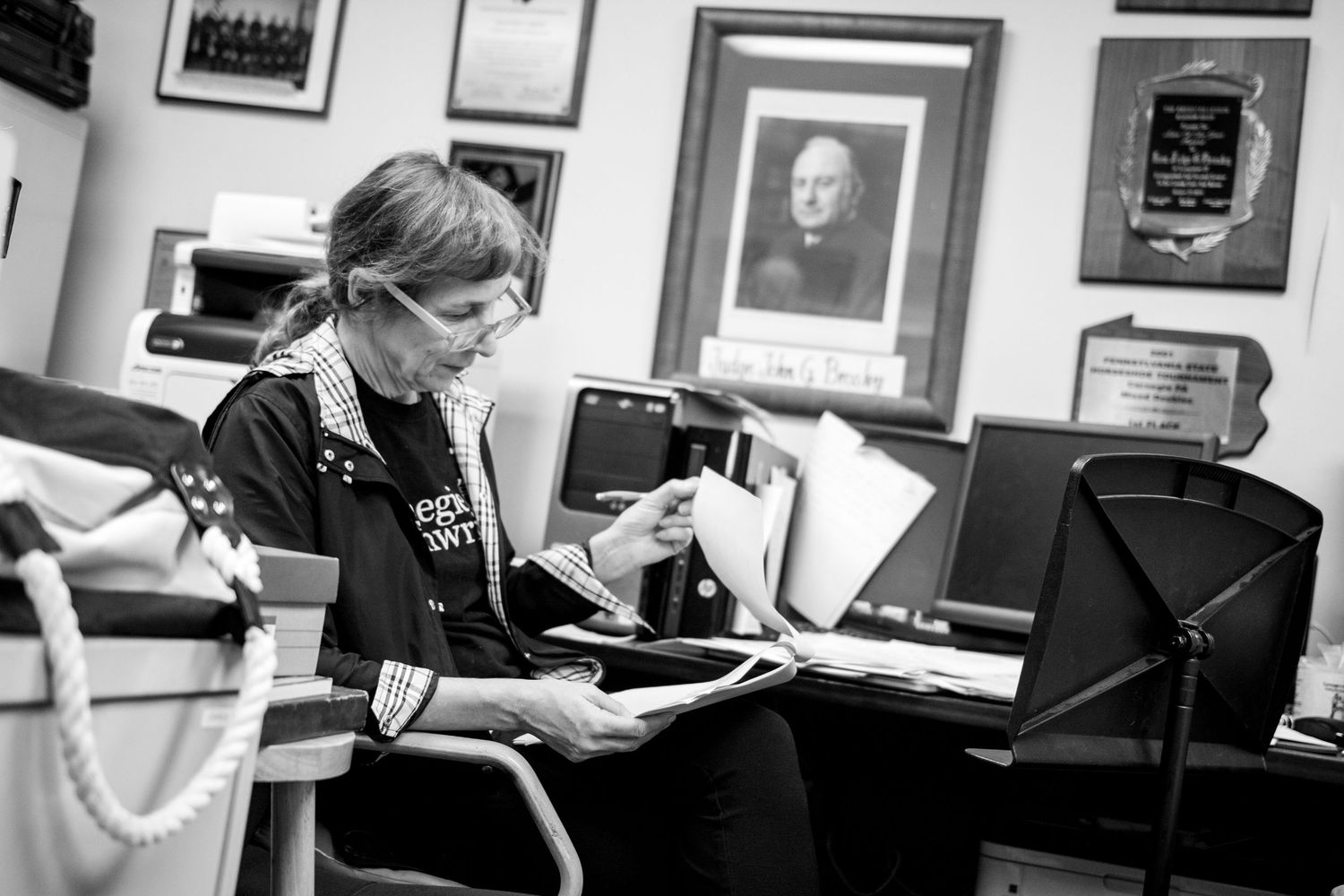 A medical professional in protective mask reviews paperwork at a desk in a black and white photograph.