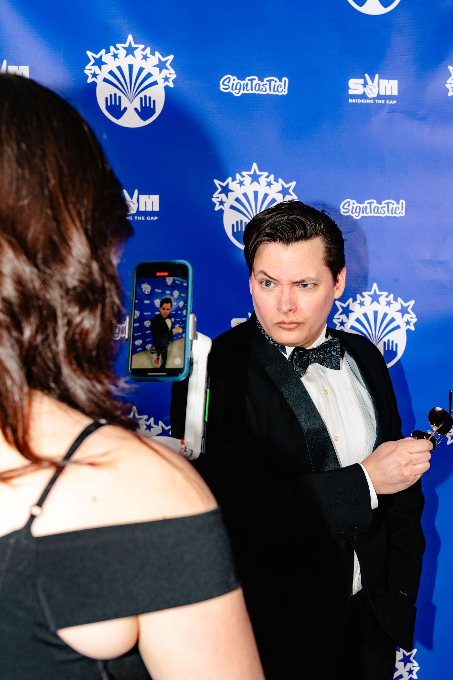 Person in formal attire poses against blue backdrop with event logos and snowflake designs.