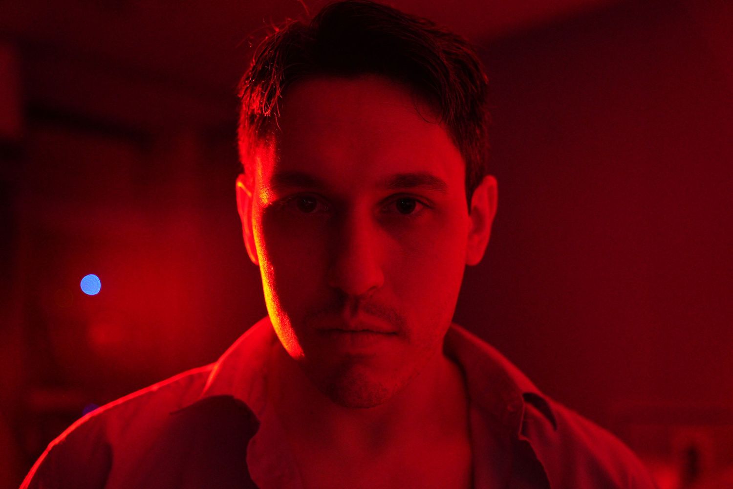 Man with serious expression bathed in dramatic red light, creating a moody cinematic portrait atmosphere.