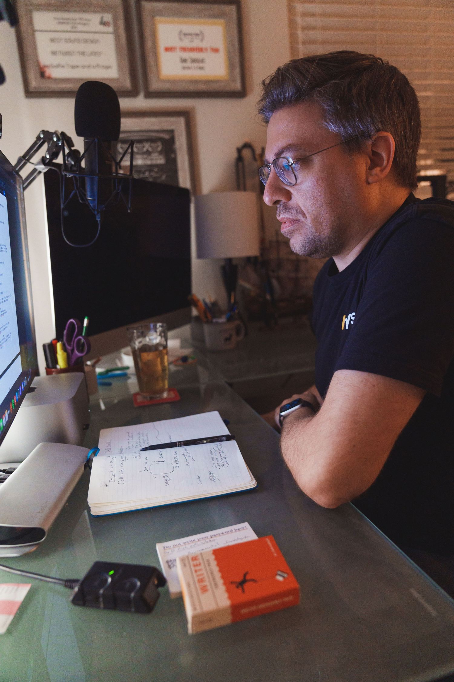 Person working at desk with multiple computer monitors and books in home office setup.
