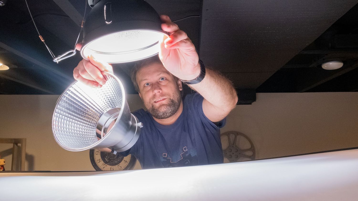 Man installing a commercial light fixture on a dark ceiling indoors.