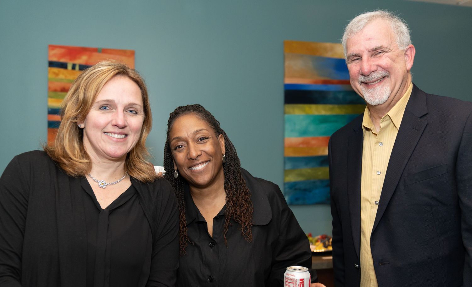 Three people pose together at an art gallery opening reception.