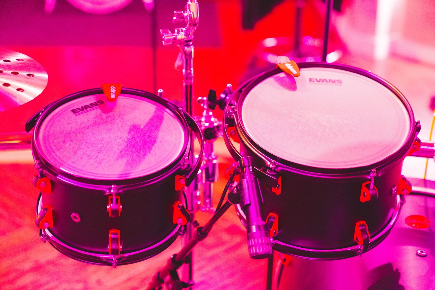 Drum kit illuminated by vibrant pink and red stage lighting.