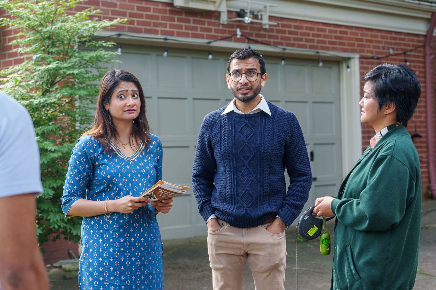 People gathered outside a house with brick walls and greenery in the background.