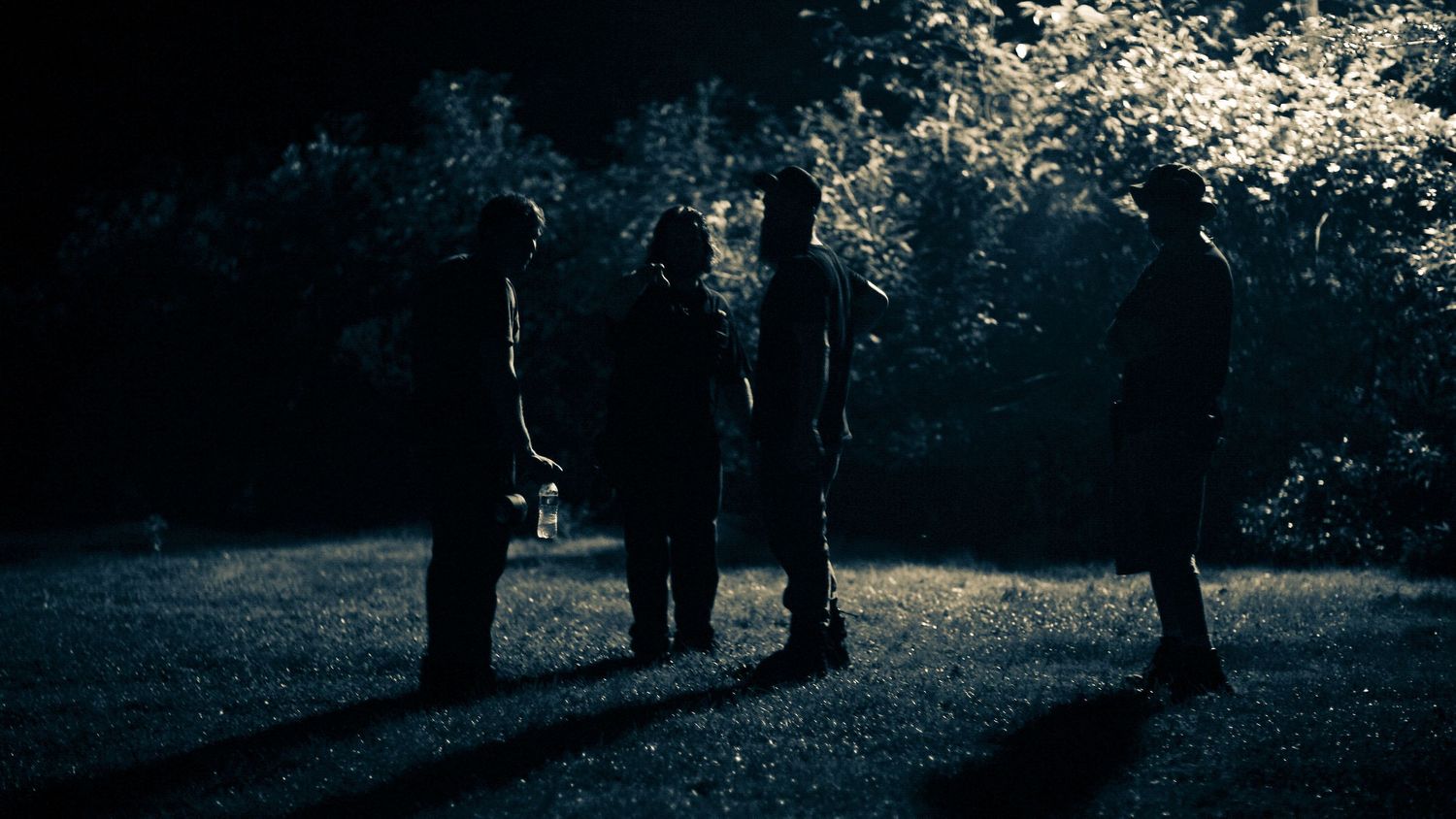 People walking in silhouette against a bright backlit outdoor setting.