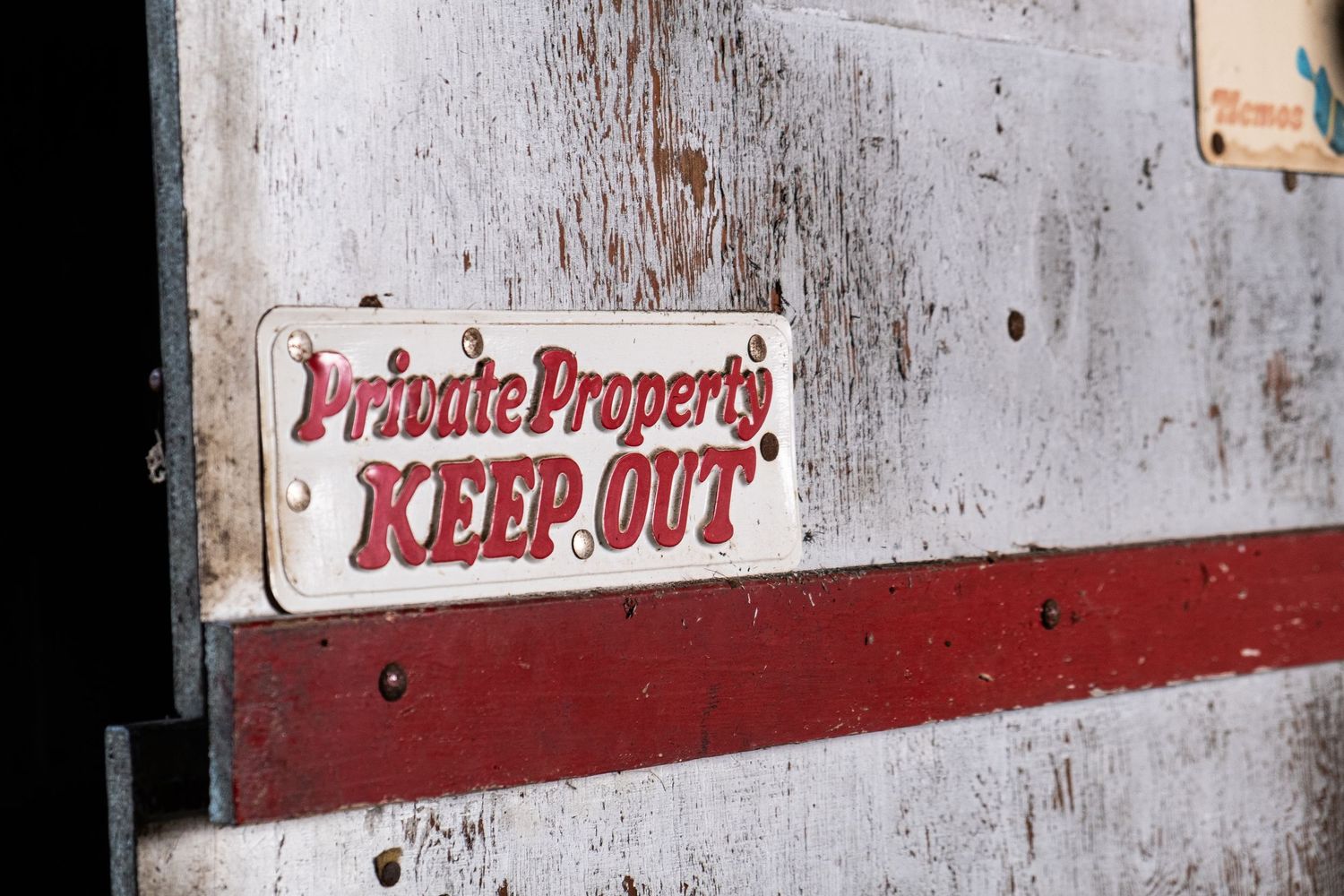 Vintage Private Property Keep Out sign on a weathered red and white wooden door or wall.