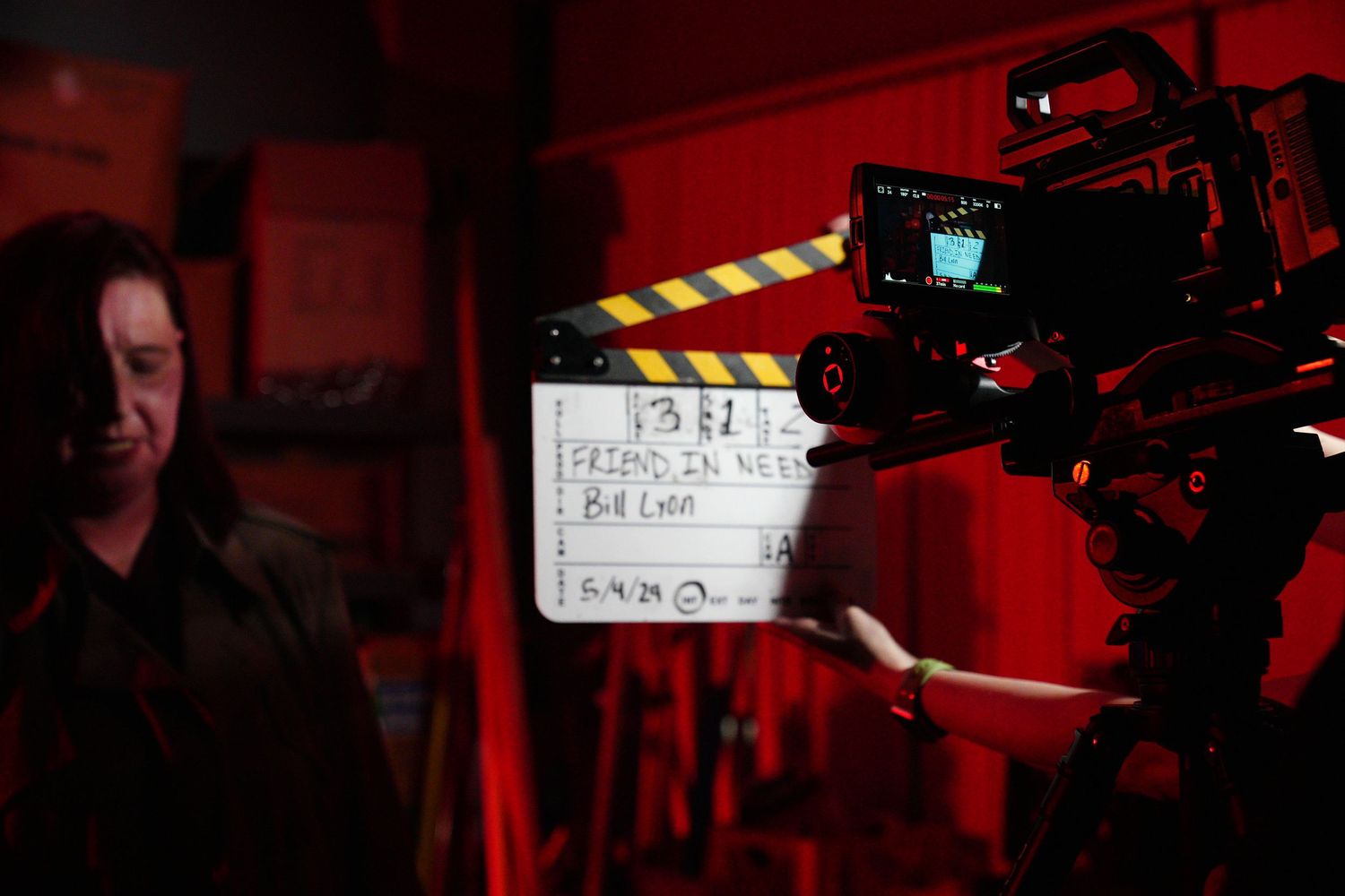 A film clapperboard is held in front of a professional camera on a red-lit movie set.