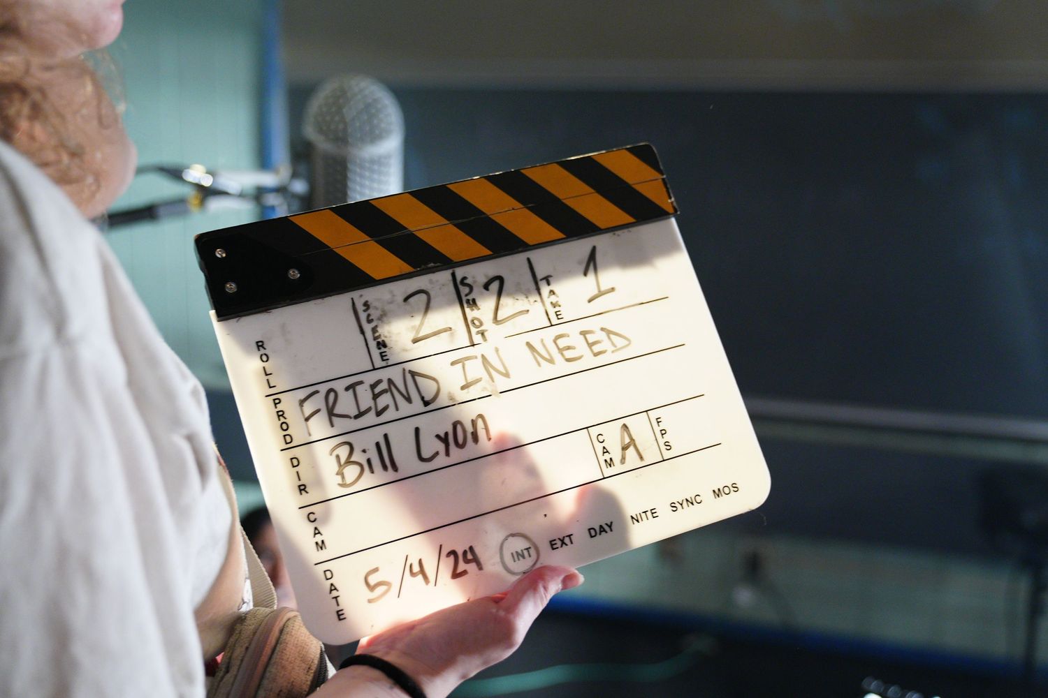 A film clapperboard reading 'Friend in Need' directed by Bill Lyon, dated 5/4/29, held on a movie set.