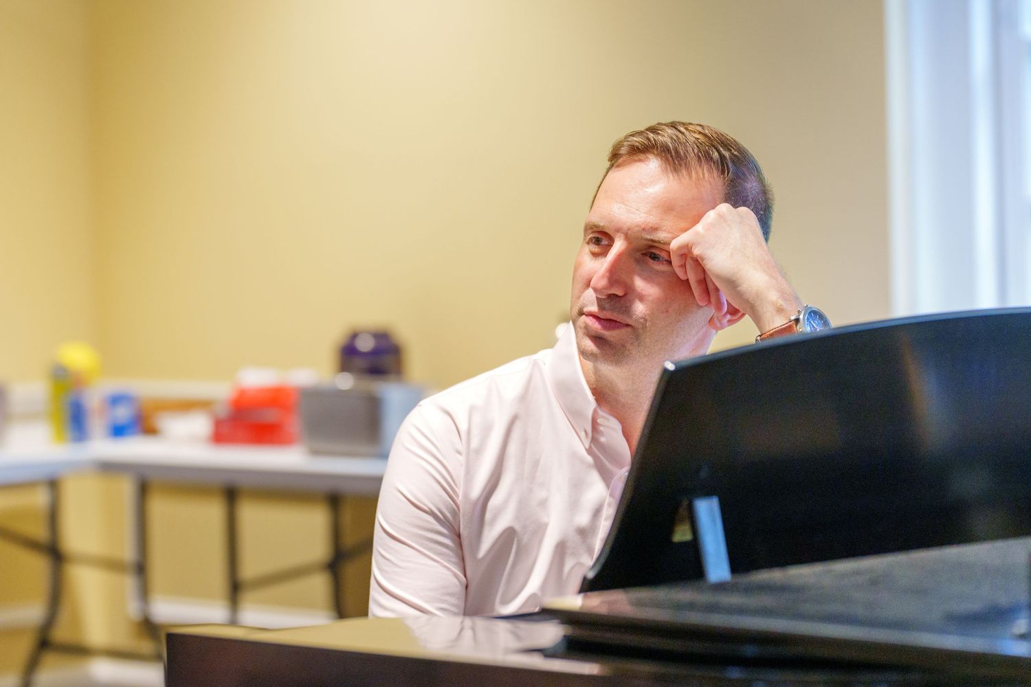 Thoughtful man in white shirt resting head on hand while looking at laptop screen in a bright room.