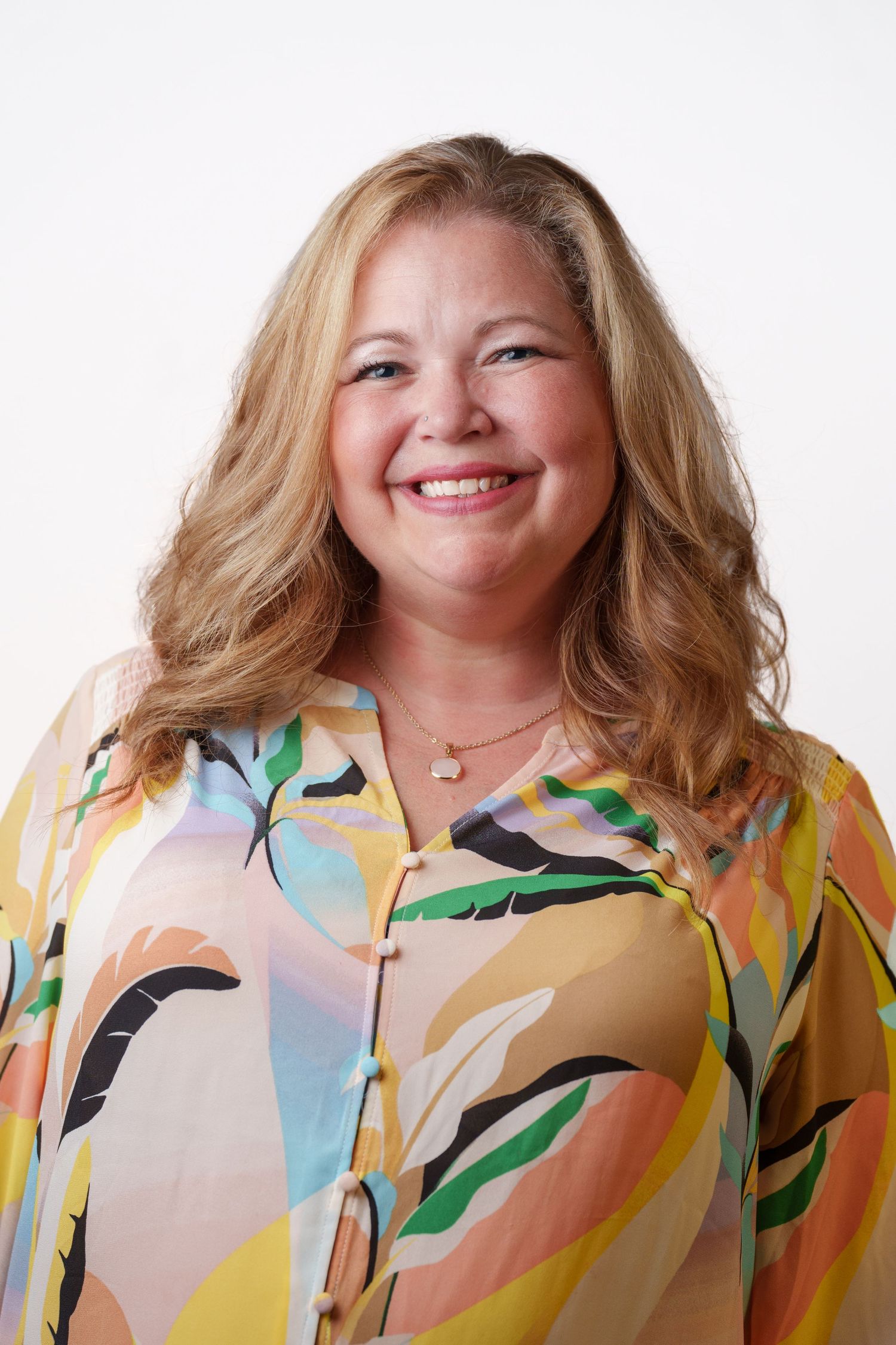 A person wearing a colorful abstract patterned blouse smiles warmly against a white background.