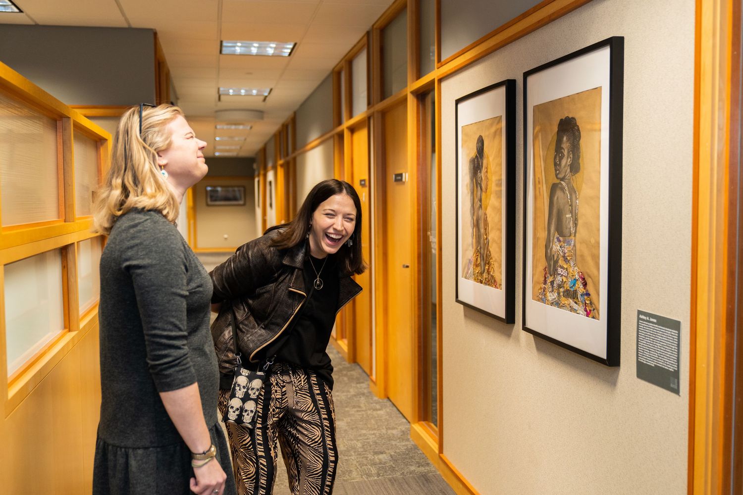 Two people admiring artwork displayed in an office hallway gallery.