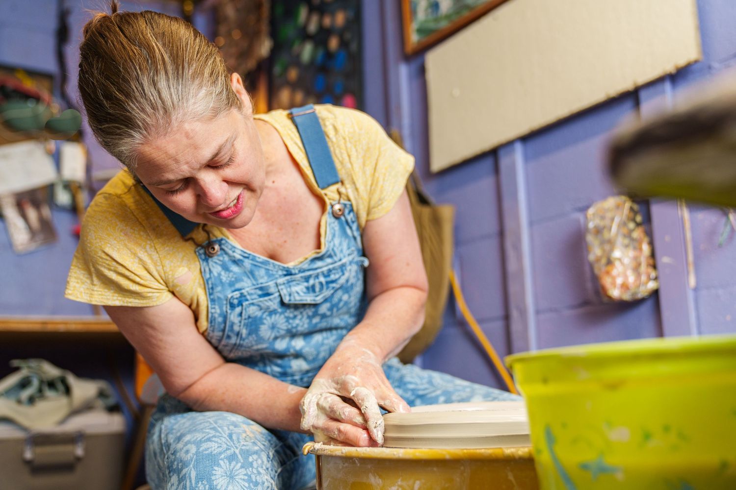 Artist works on pottery wheel in studio while shaping clay with hands and tools.