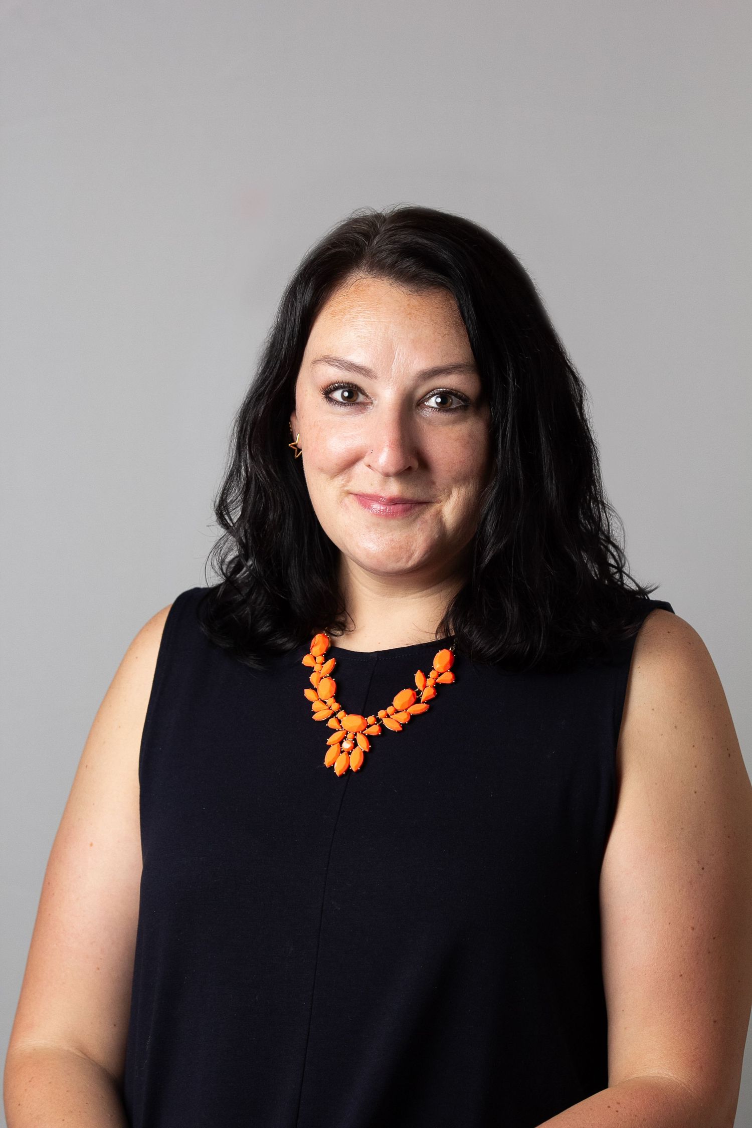 A series of headshots showing a person in a black sleeveless top wearing a bright orange statement necklace.