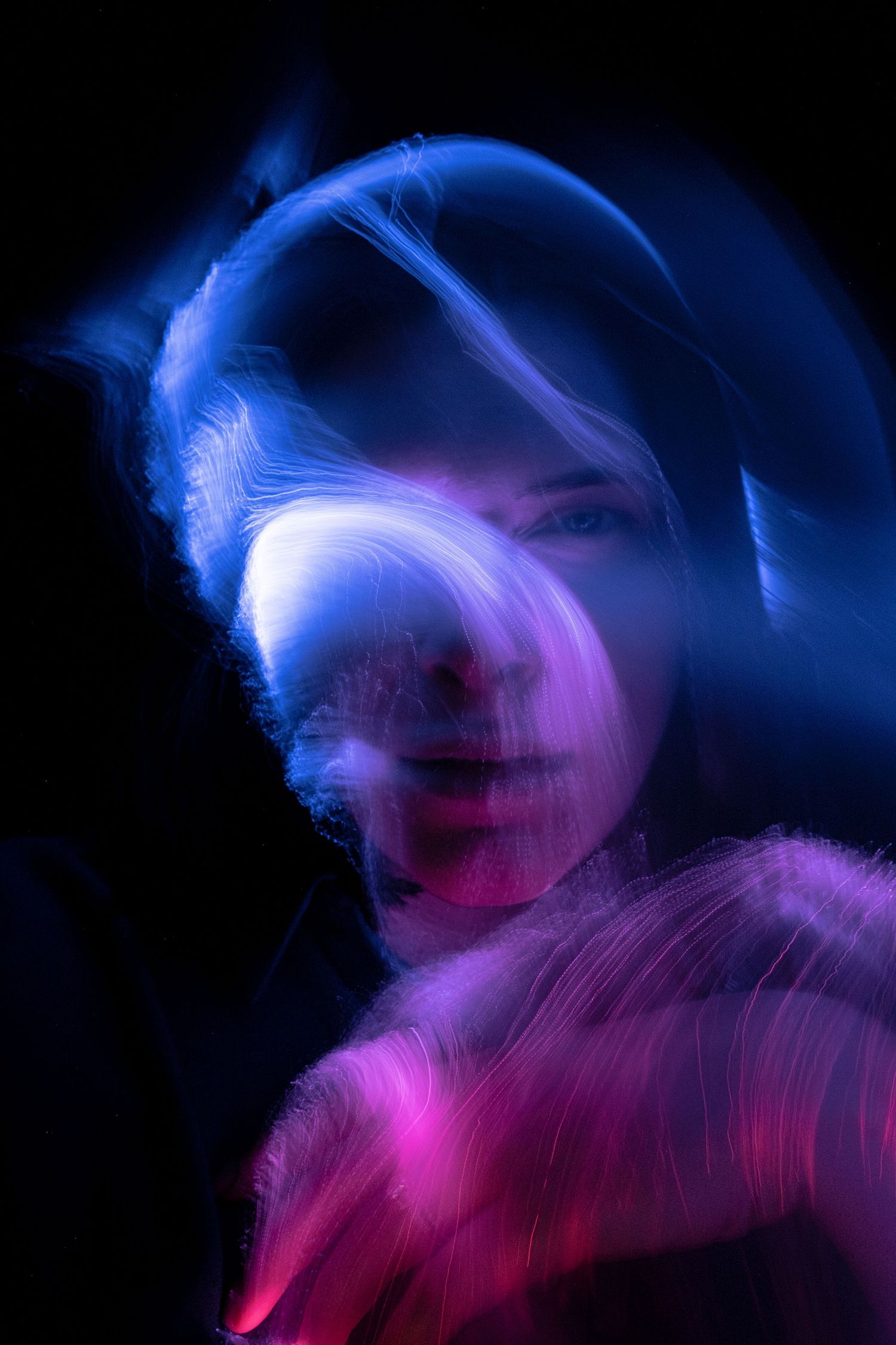 Abstract portrait with motion blur creating ethereal blue and pink light trails against dark background.