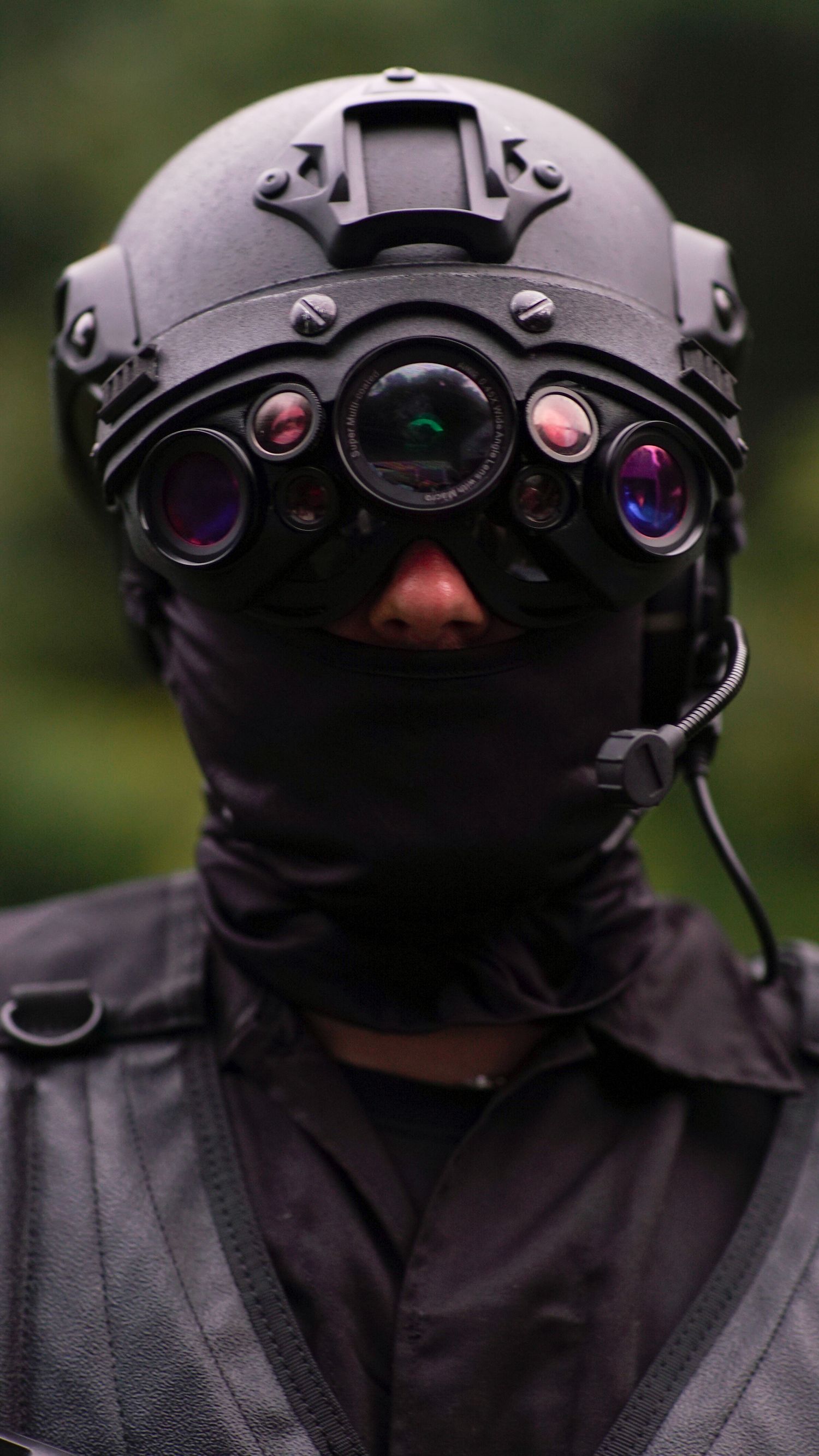 Military operator wearing advanced night vision goggles mounted on tactical helmet with black balaclava and headset.