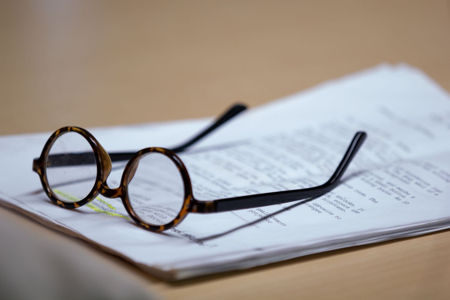 Round tortoiseshell glasses resting on printed documents on a wooden desk.