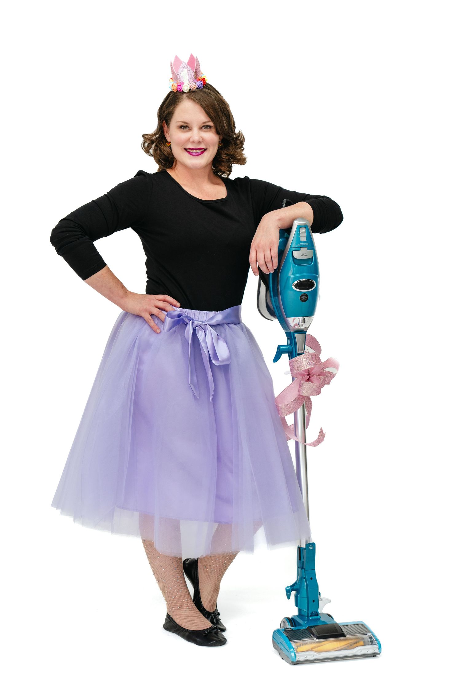 Playful portrait with purple tulle skirt and blue vacuum cleaner against white background.