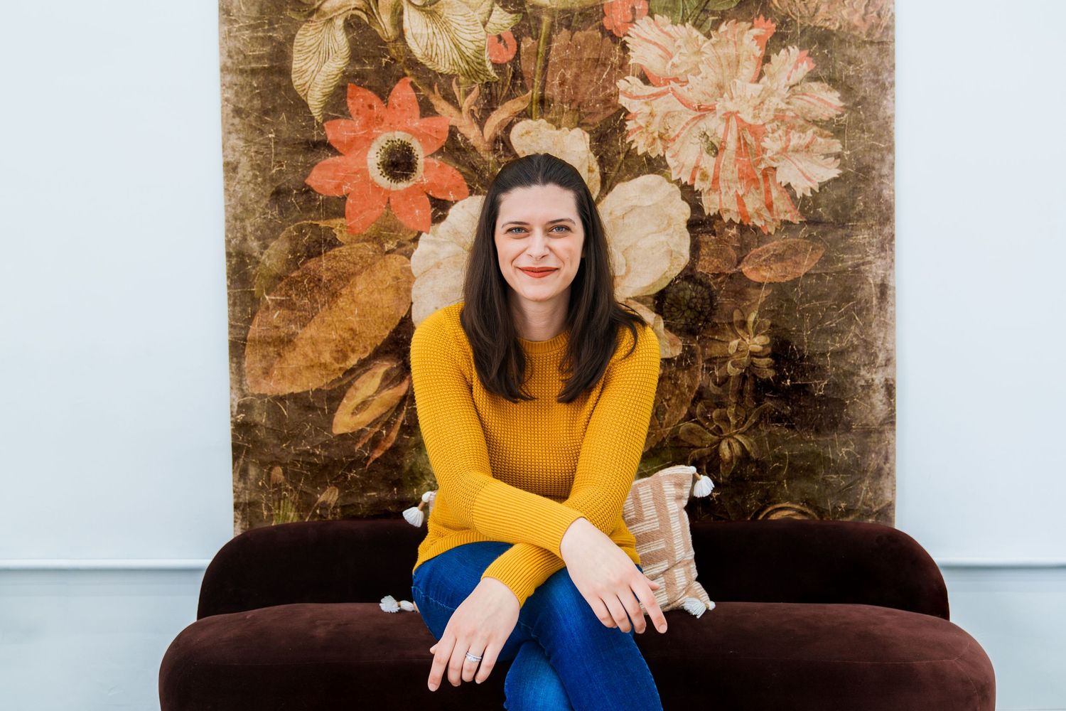 Person in mustard sweater sitting on brown couch in bright room.