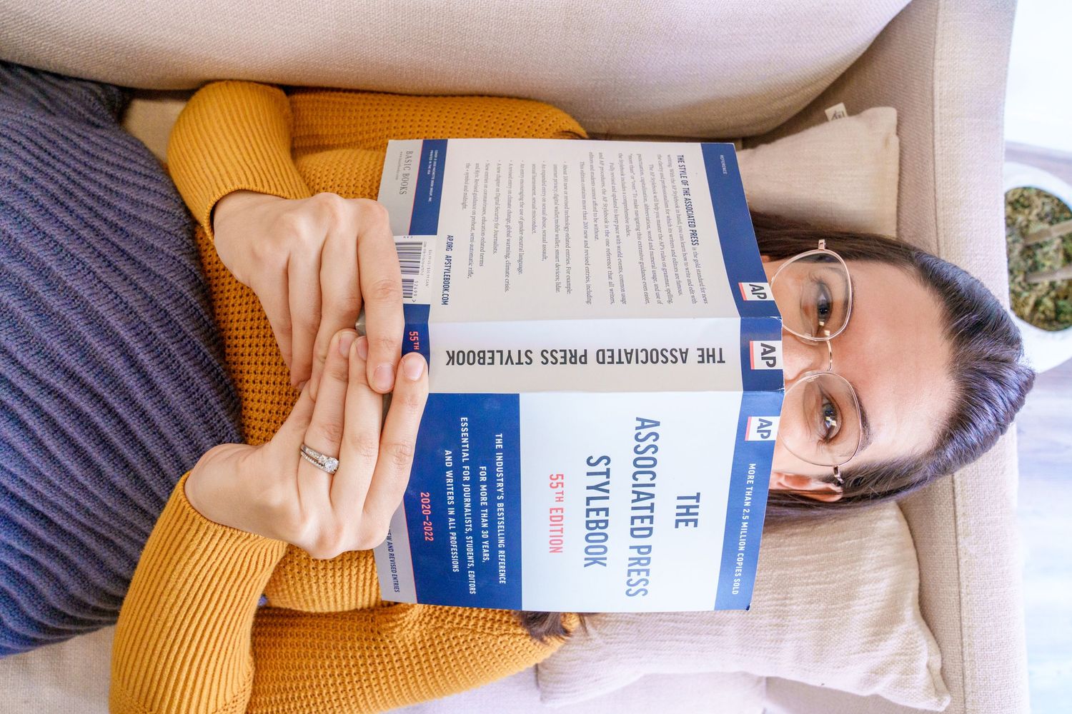 Book being held while resting on white couch with yellow sweater visible.