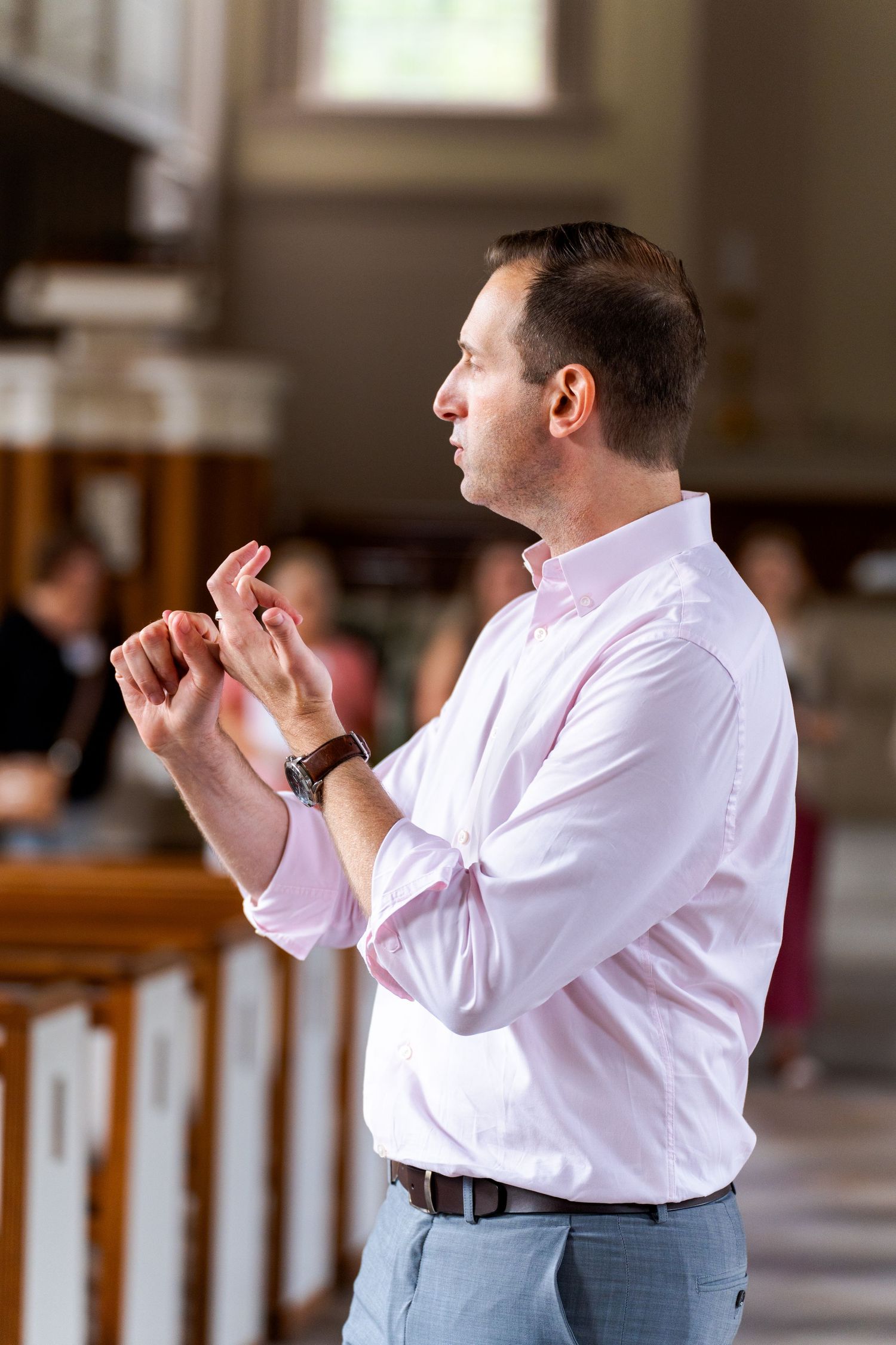 Man in pink shirt speaking passionately in a church setting, gesturing with hands raised.