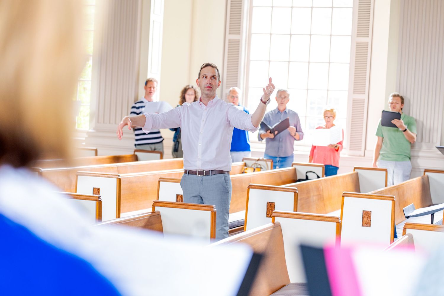 Congregation members raising hands in worship during a church service in a bright sanctuary with wooden pews.