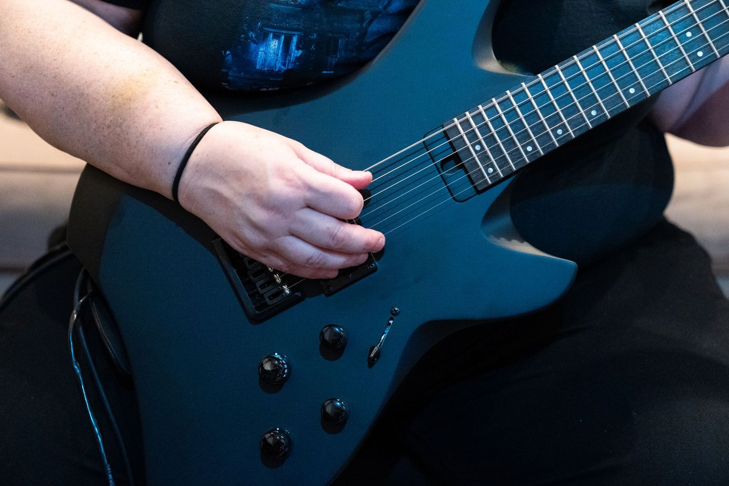Close-up shot of hands playing a black electric bass guitar against dark background.