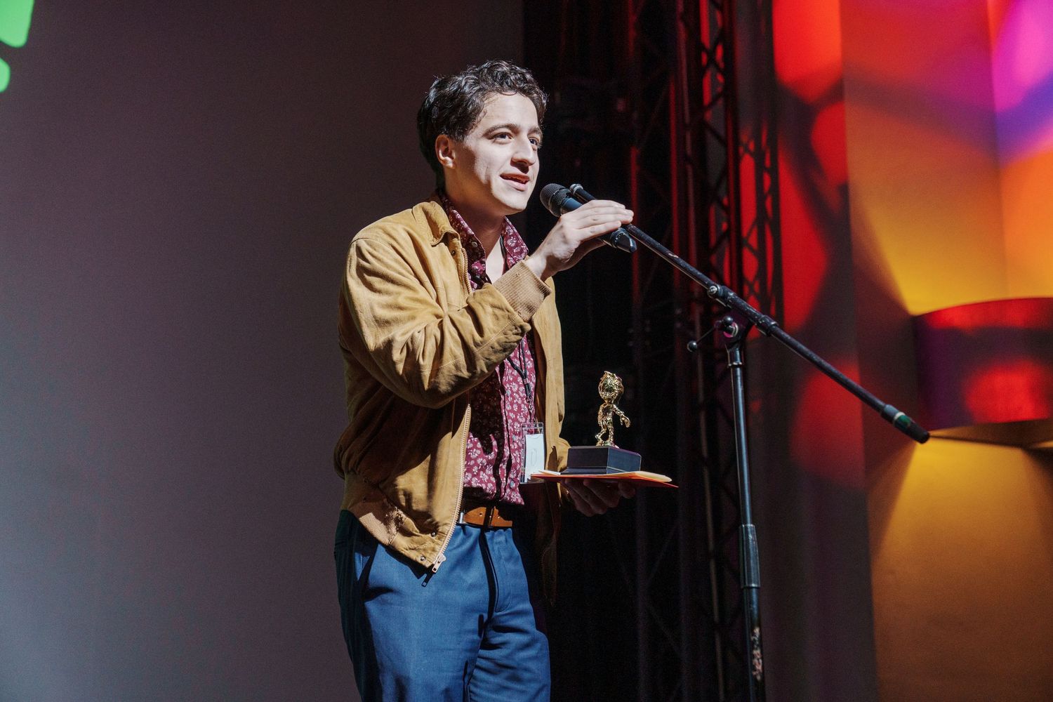 Stage performer in casual attire under dramatic red and orange lighting.