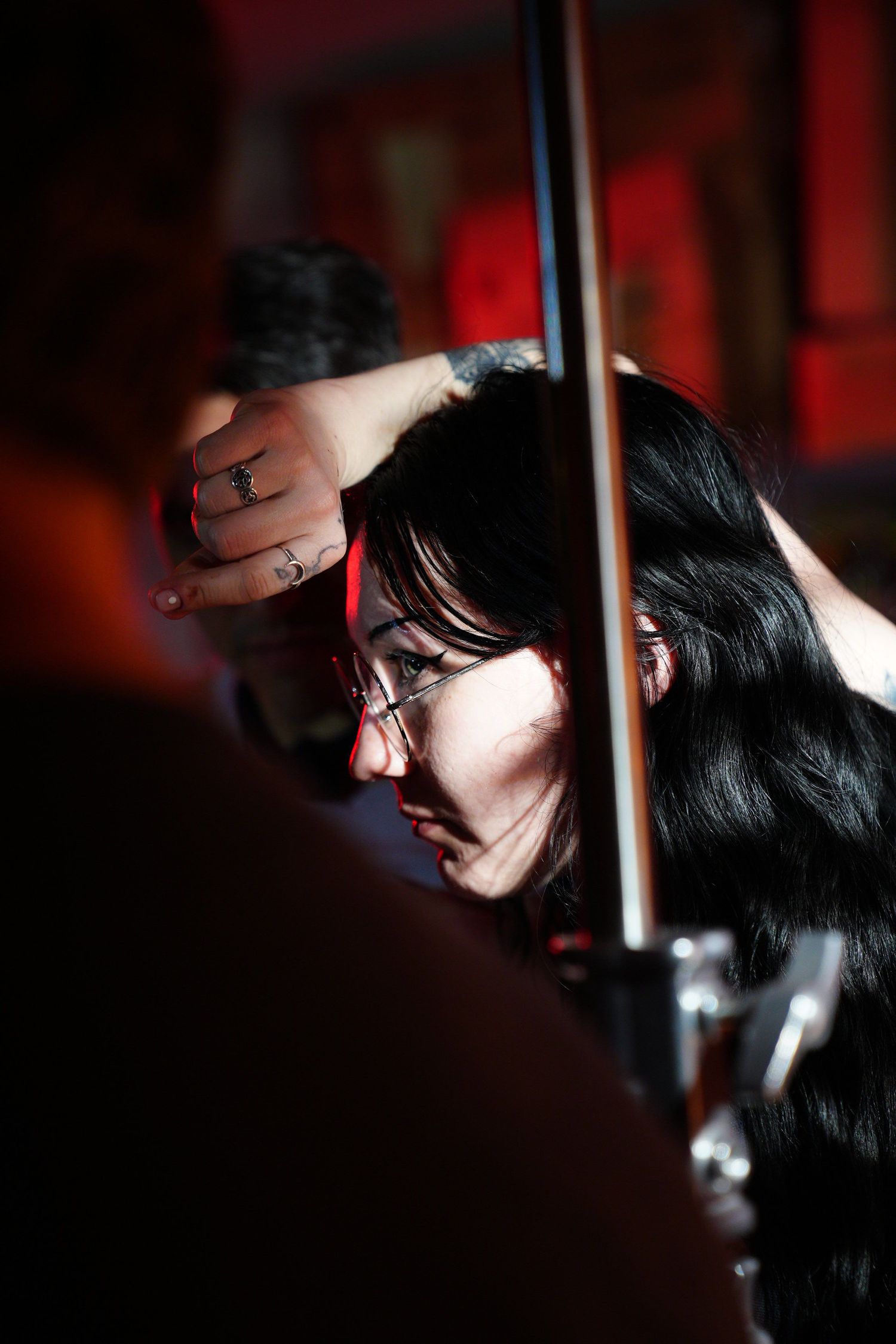Young woman with black hair and glasses playing violin under dramatic red stage lighting.