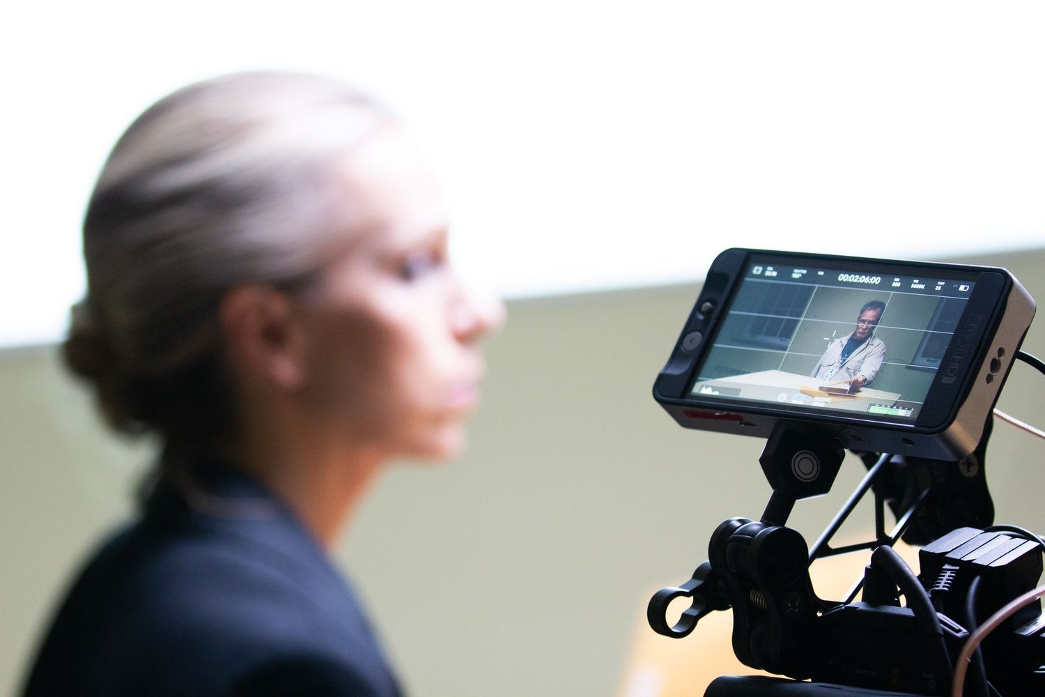A woman being filmed on a professional video camera with a monitor displaying her image on a studio set.