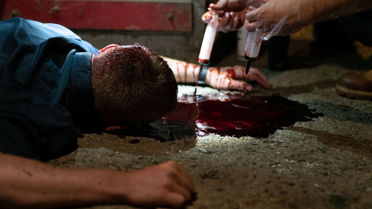 Special effects crew applies fake blood makeup to an actor lying on a floor on a film set.