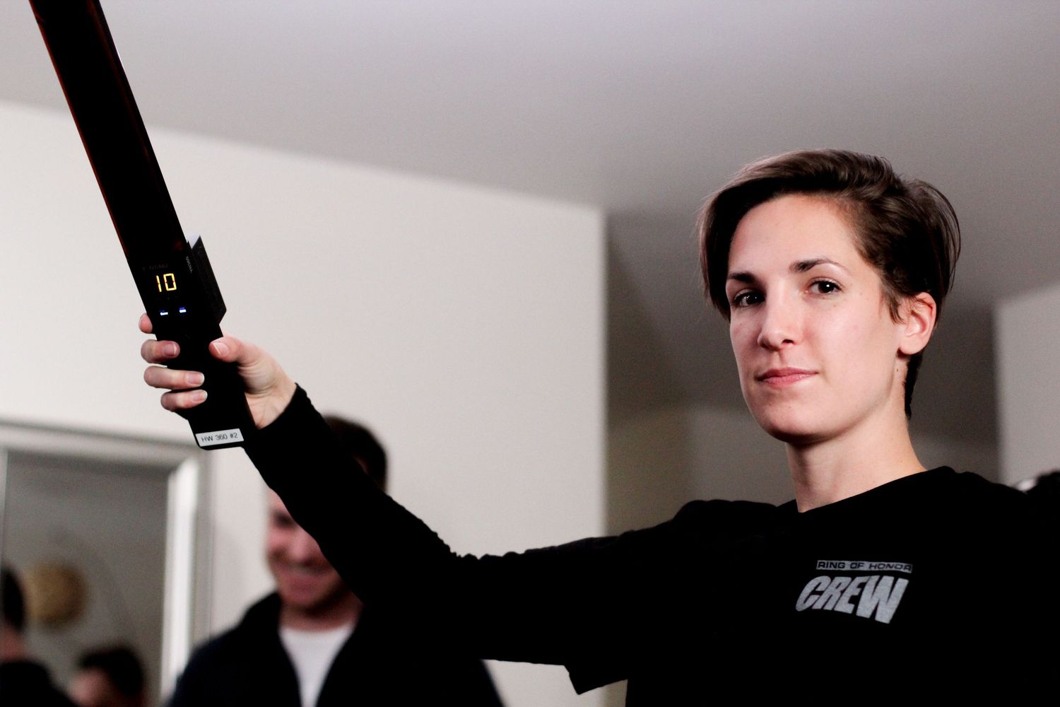 Woman in black crew sweatshirt holding a boom microphone pole on a film set.