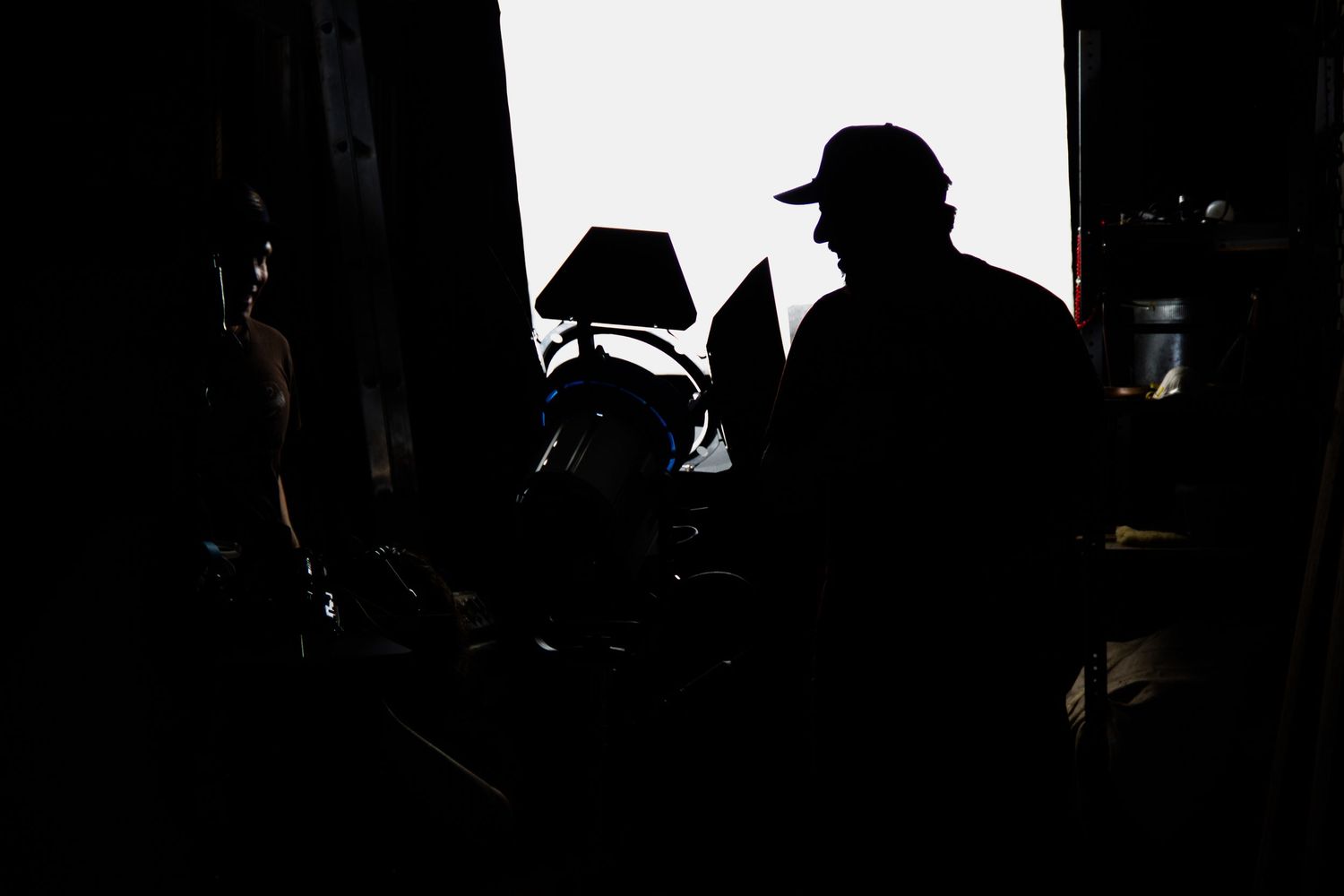 Silhouette of a person wearing a cap surrounded by equipment in a dimly lit workspace.
