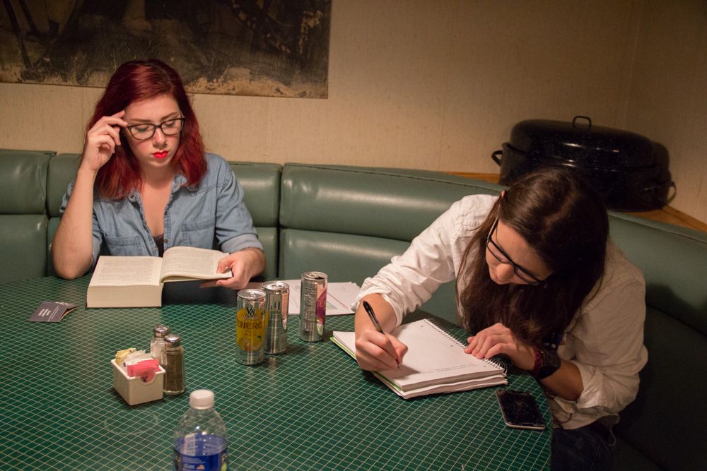 Two women study and take notes while sitting in a green booth at a diner.