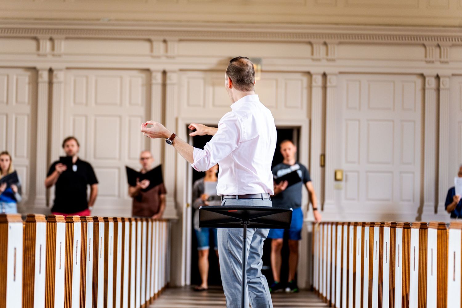 People gathered in an elegant room with white paneled walls and wooden railings.