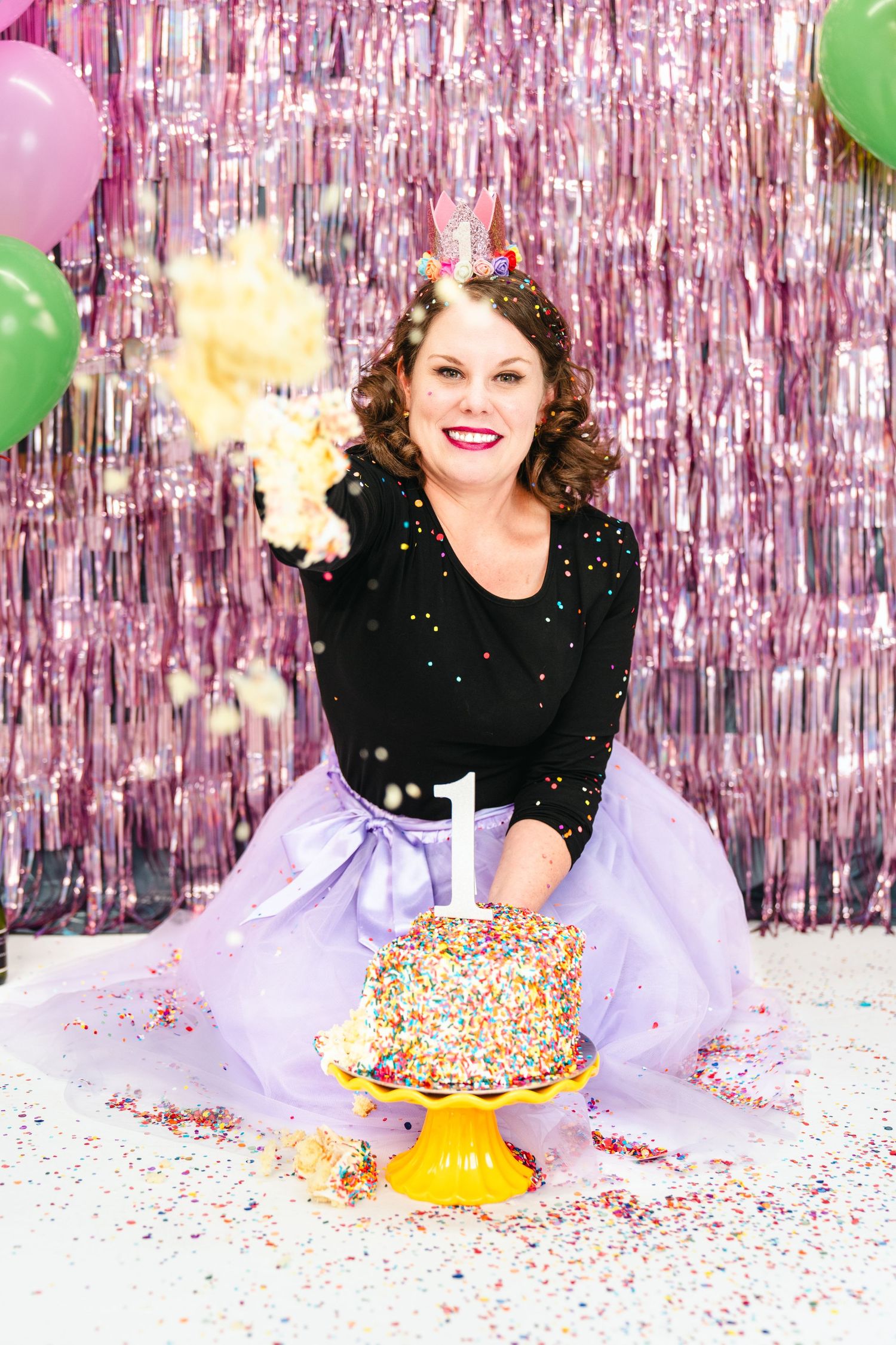 Festive party setup with tulle skirt, sparkly cake, pink metallic backdrop and green balloons.
