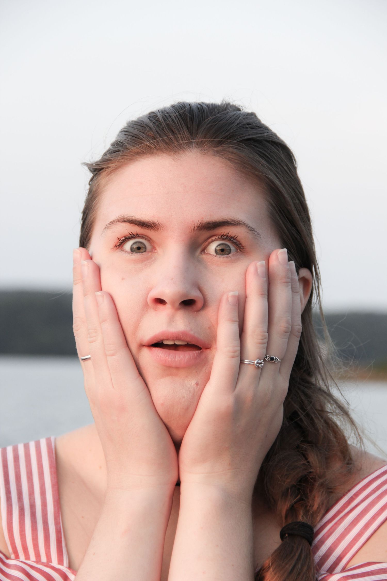 Person in red and white striped top showing surprised expression with hands on cheeks.