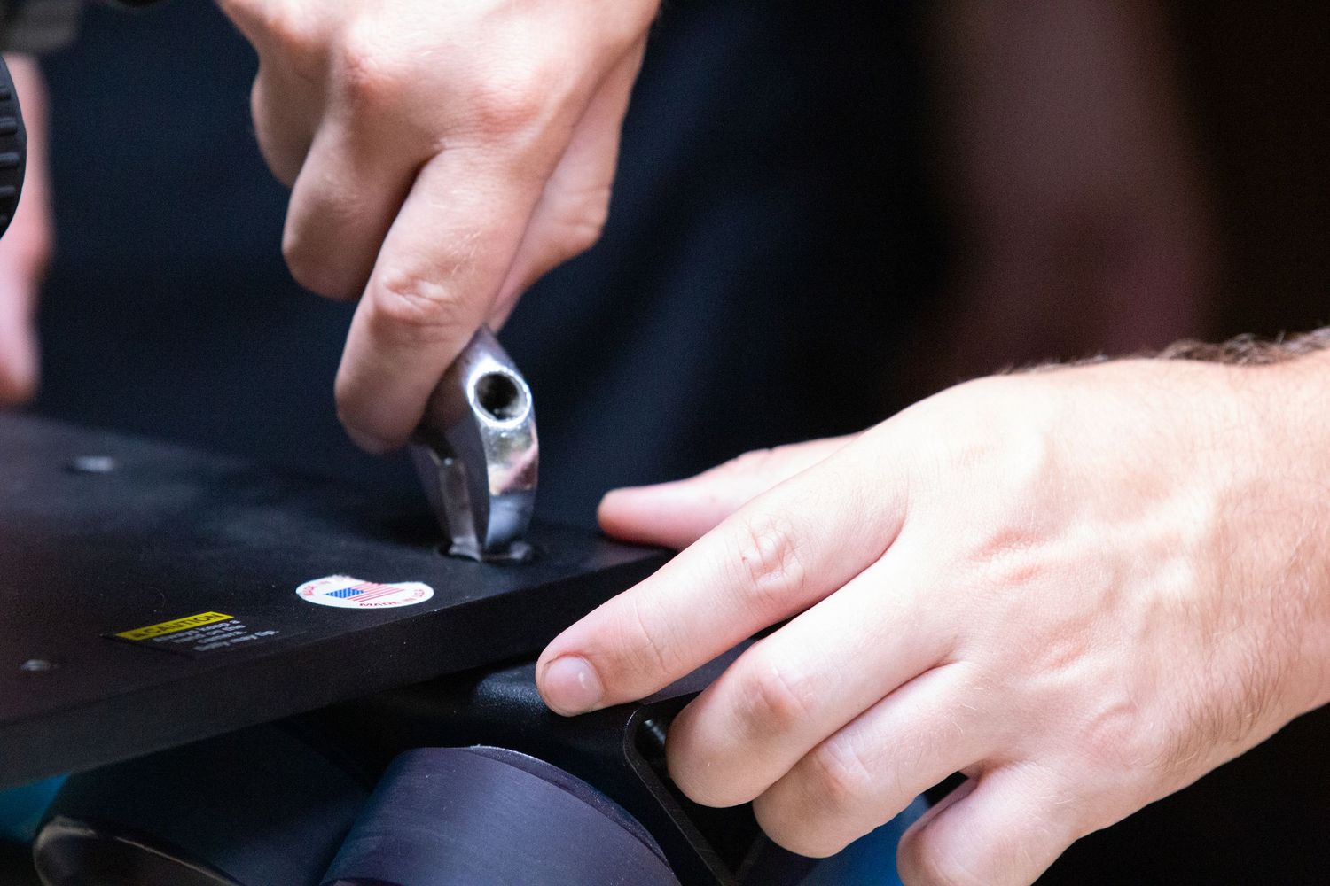 Close-up of hands using a tool to adjust a ski binding on a black ski during maintenance.