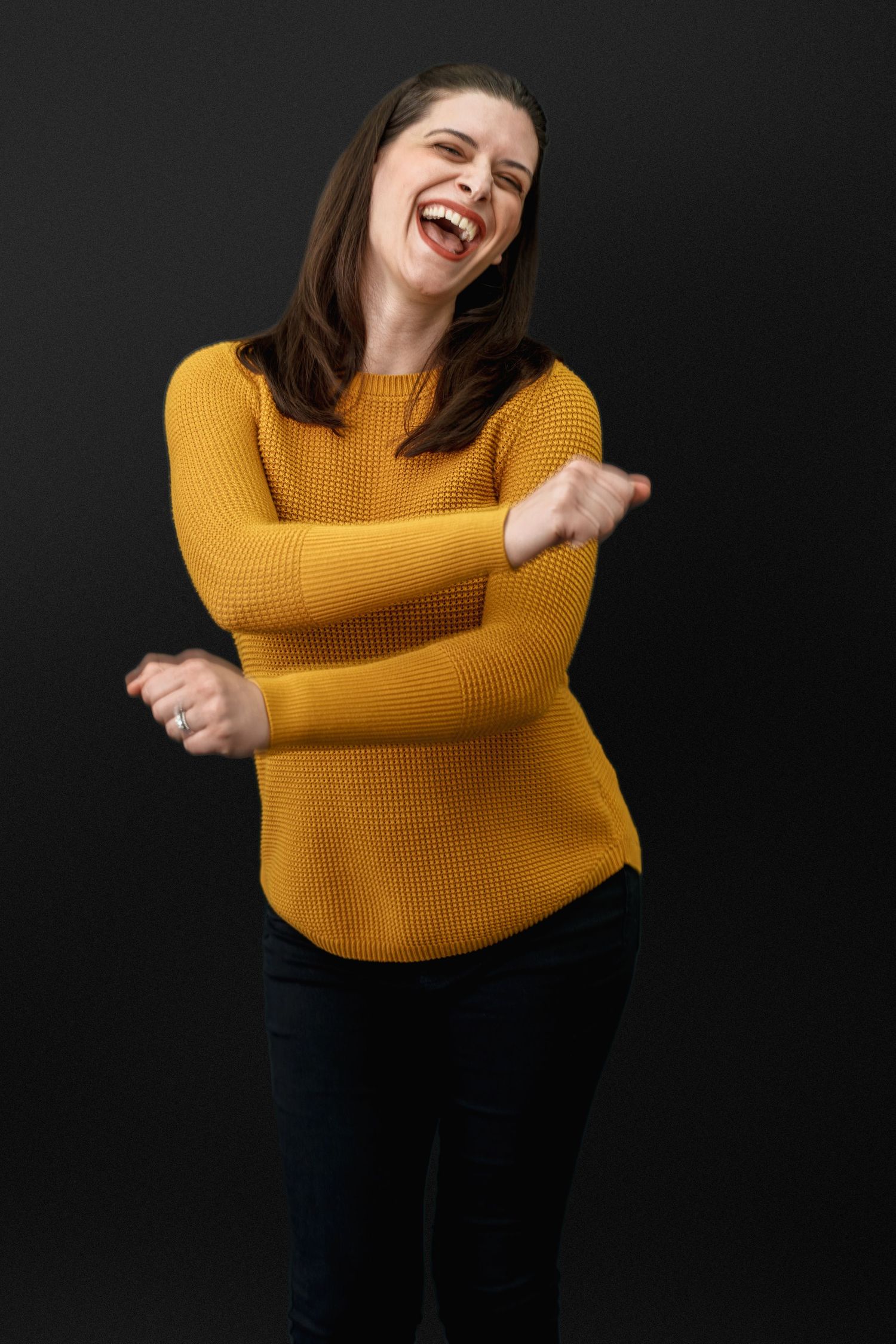 Person in yellow sweater making expressive gestures against dark background.