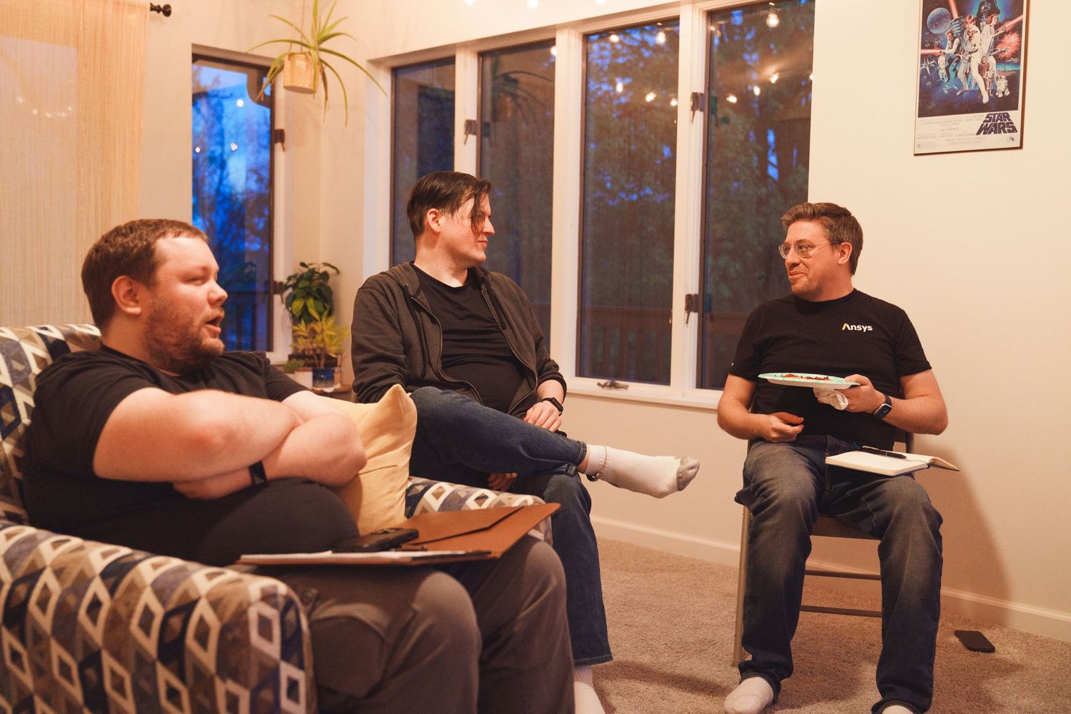 Three people having a casual conversation while sitting on a couch in a living room.