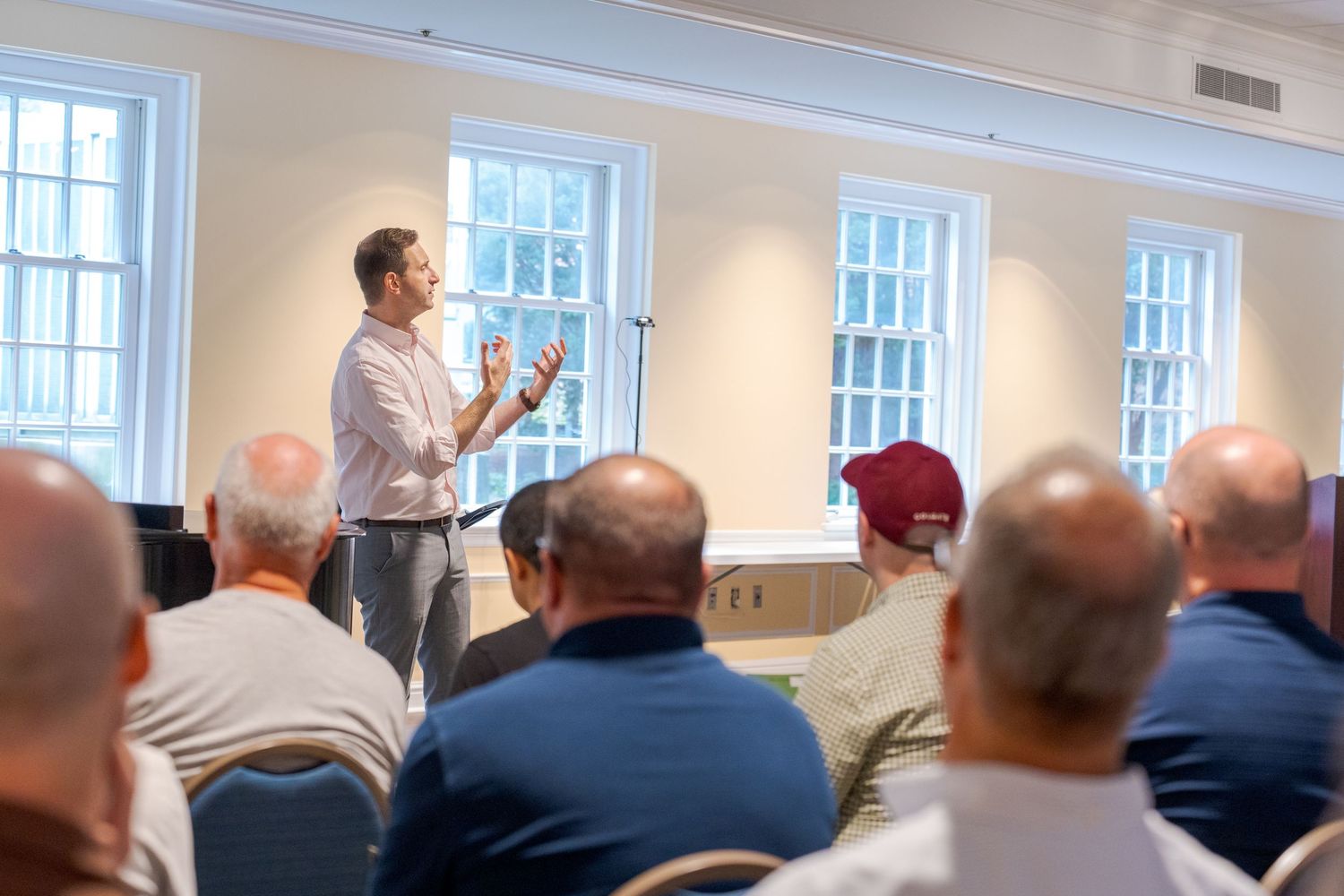 Man presenting to a seated audience in a bright conference room with large windows.