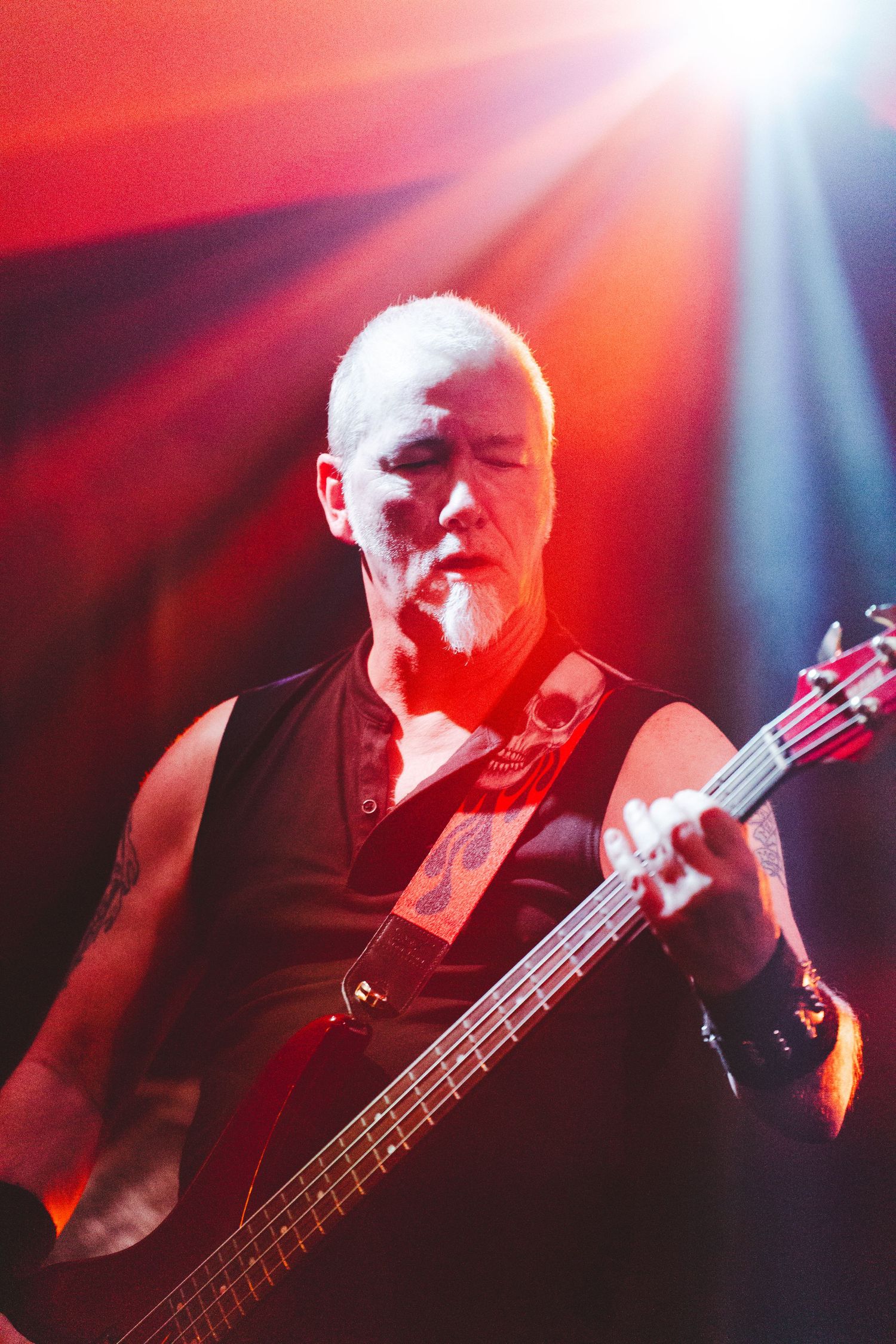 Bass guitarist performs on stage with dramatic red lighting and lens flare effects during a concert performance.