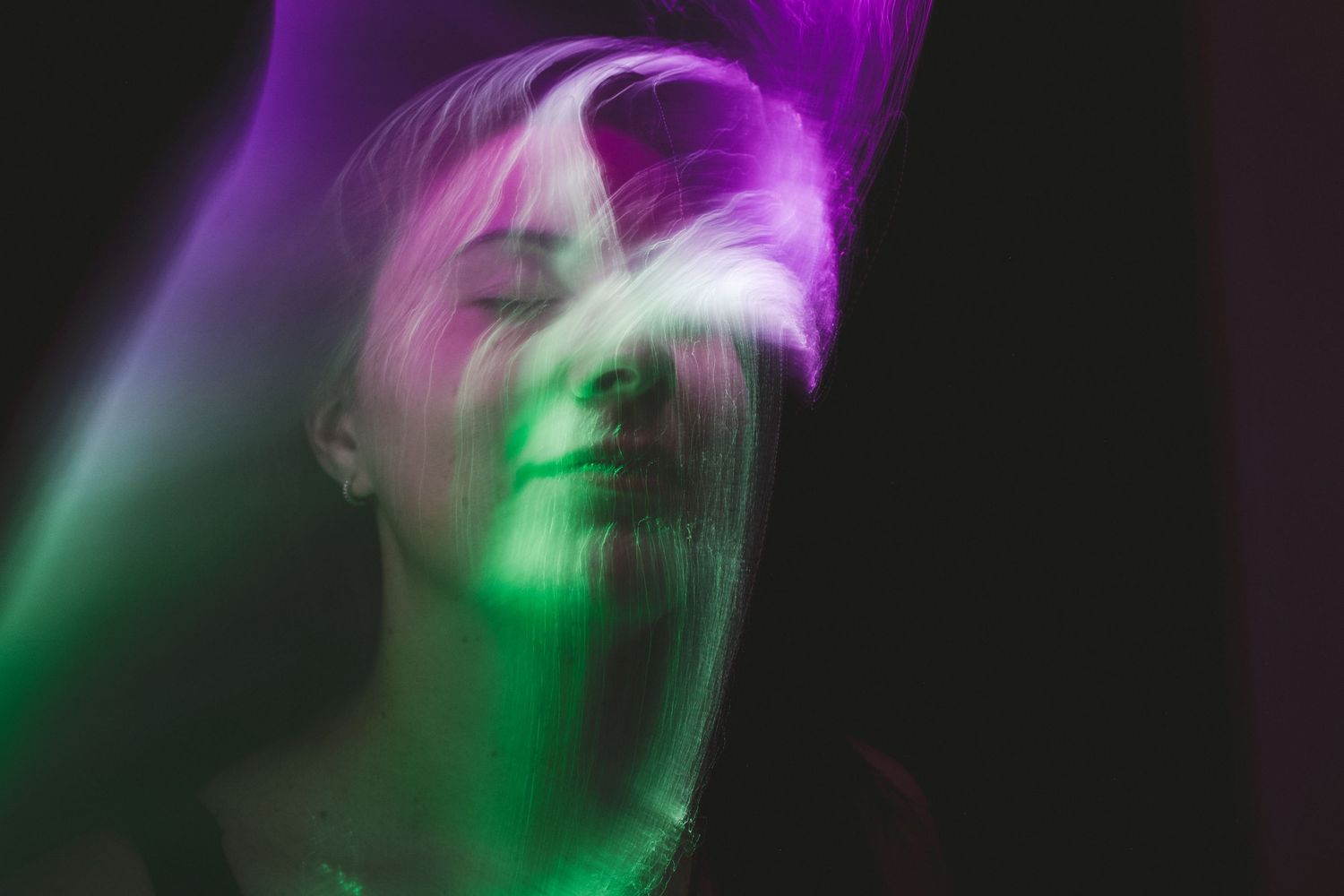 Dynamic purple and green light painting photograph with motion blur effects.