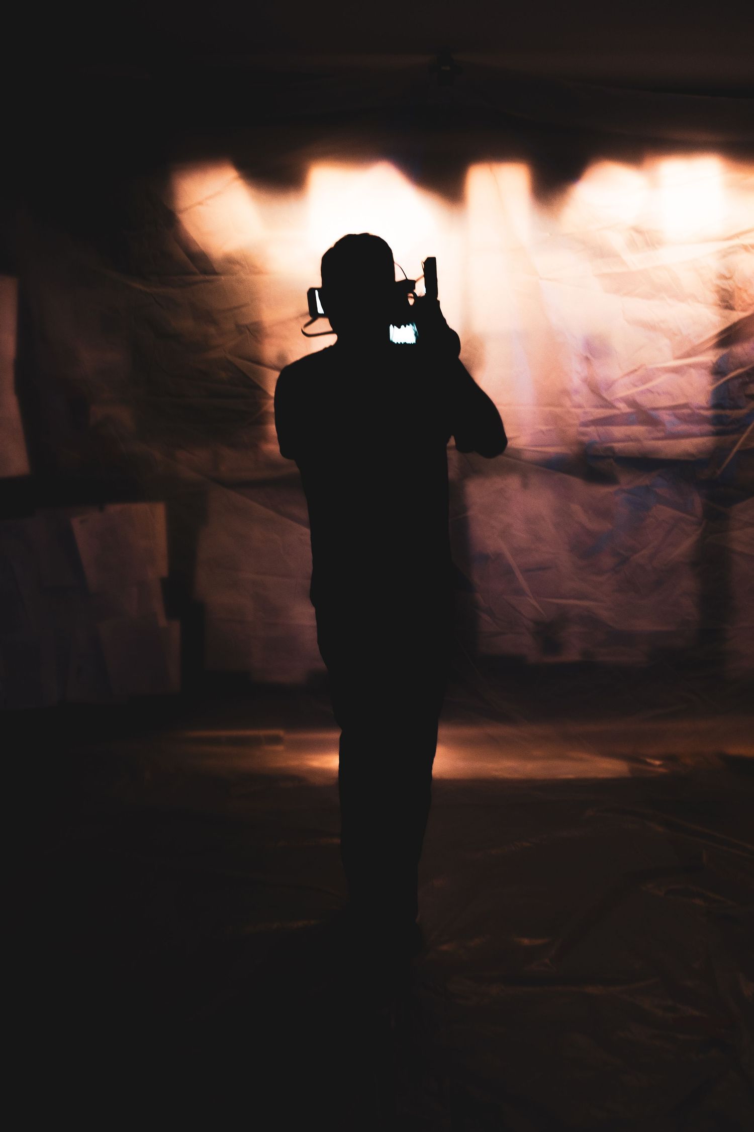 Silhouettes of camera operators filming against a dramatic smoky background with orange lighting.