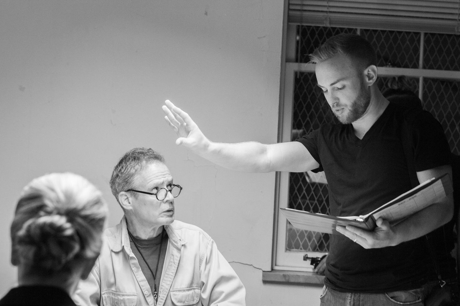 Black and white photo of two men in discussion, one gesturing with raised hand while holding a folder.