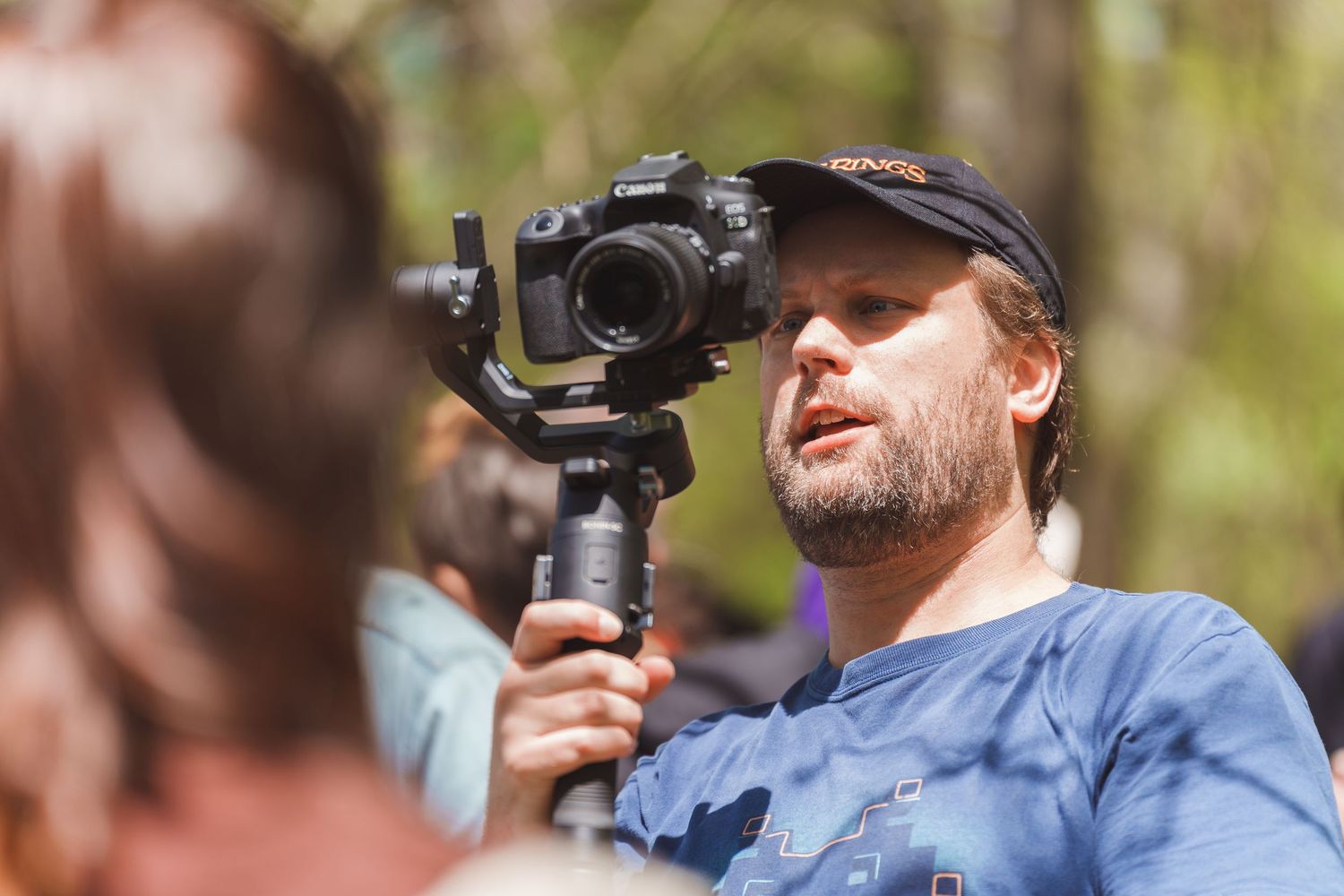 Man holding a camera gimbal stabilizer while filming outdoors in a forest setting.