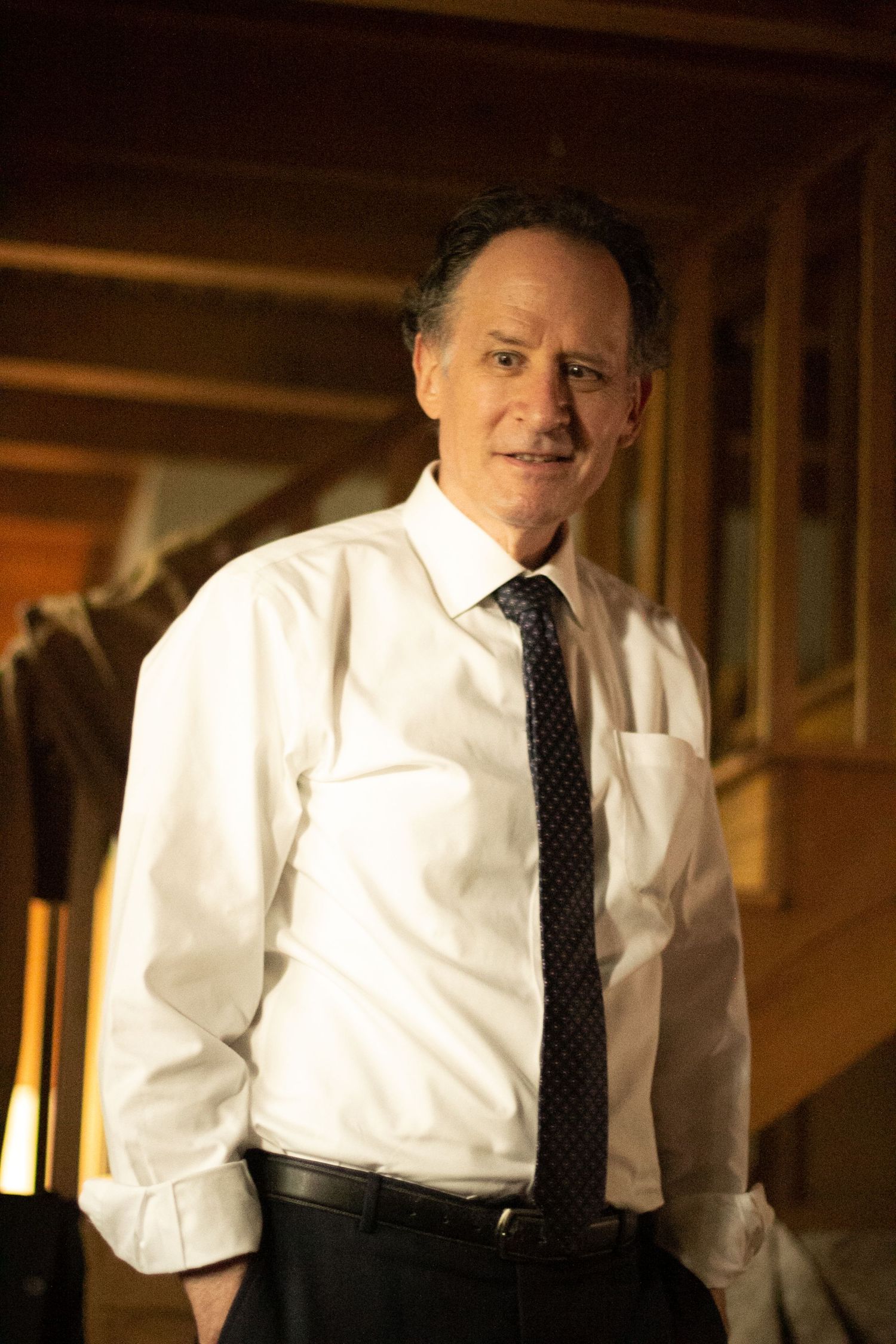 Middle-aged man in white dress shirt and dark tie smiling confidently in warmly lit wooden interior.