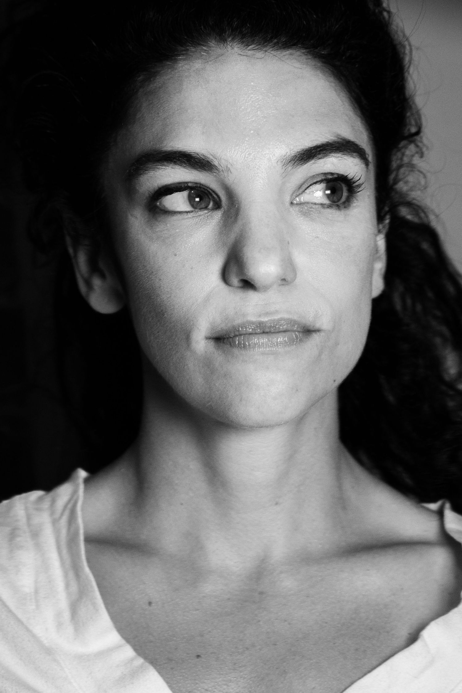 Black and white portrait of a young woman with curly hair gazing sideways, wearing a white top.