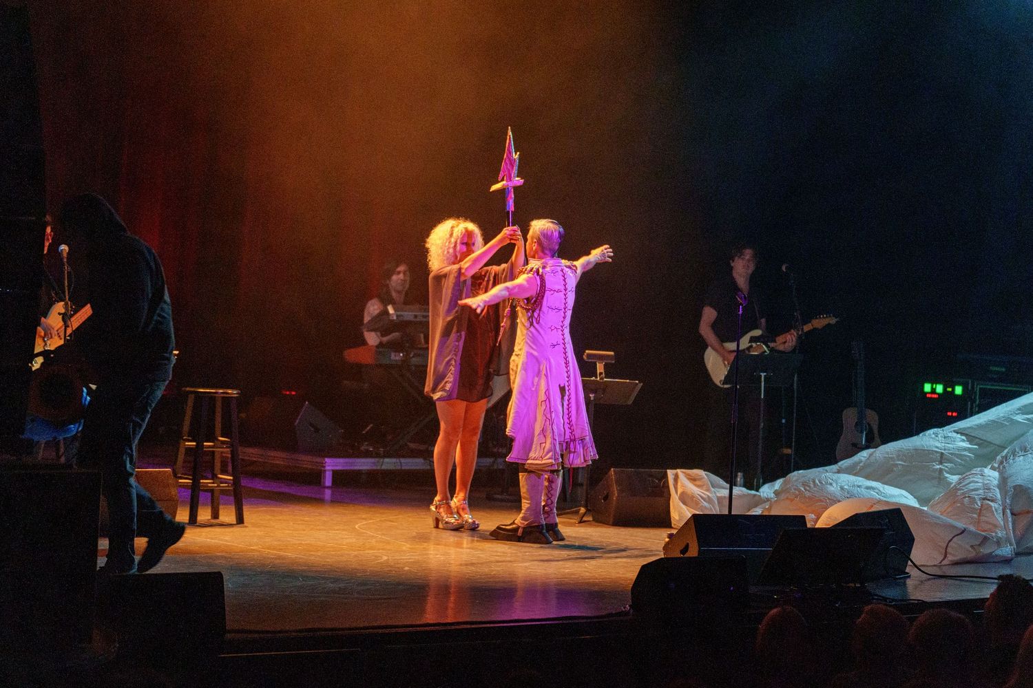 Stage performance with dramatic lighting showing silhouettes of performers in theatrical setting.