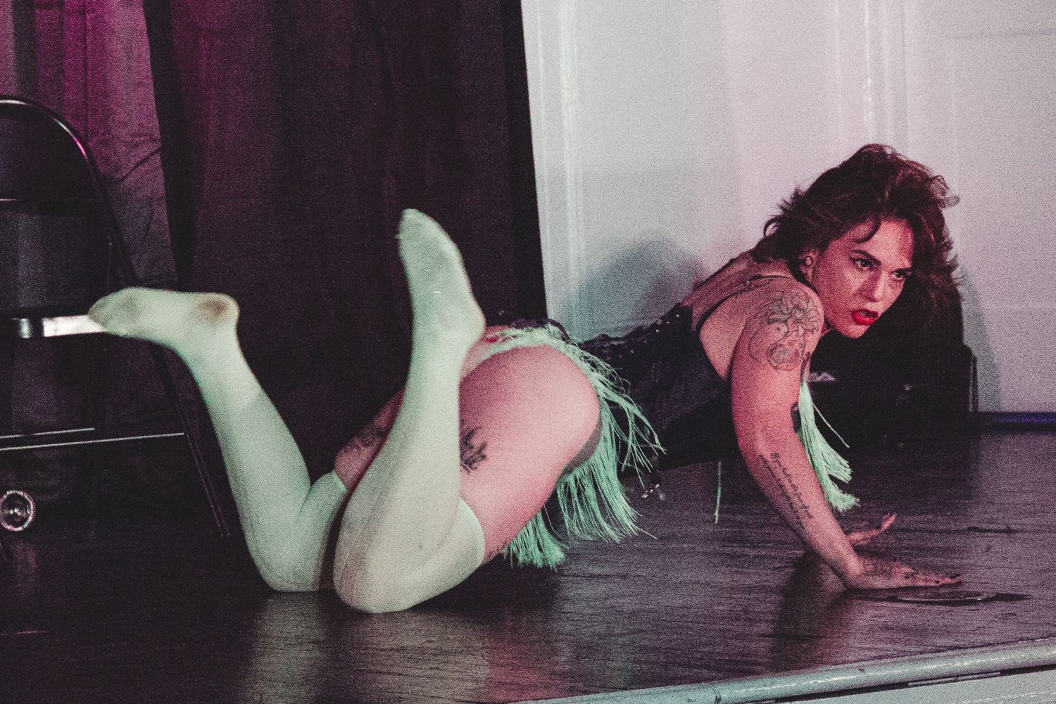 Burlesque performer in mint green lingerie poses on dark stage floor.