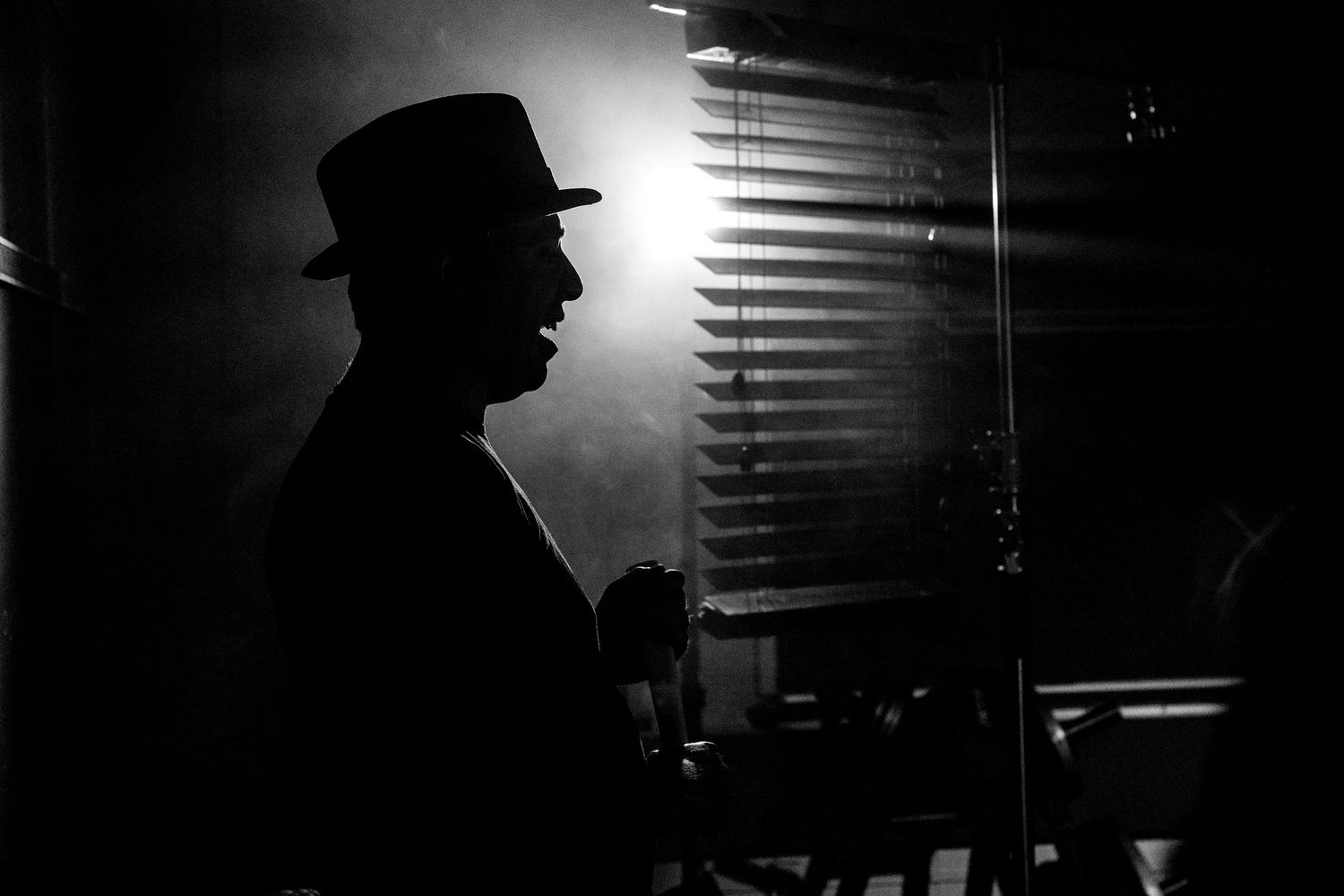 Film noir style silhouettes with venetian blind shadows creating dramatic lighting effects.